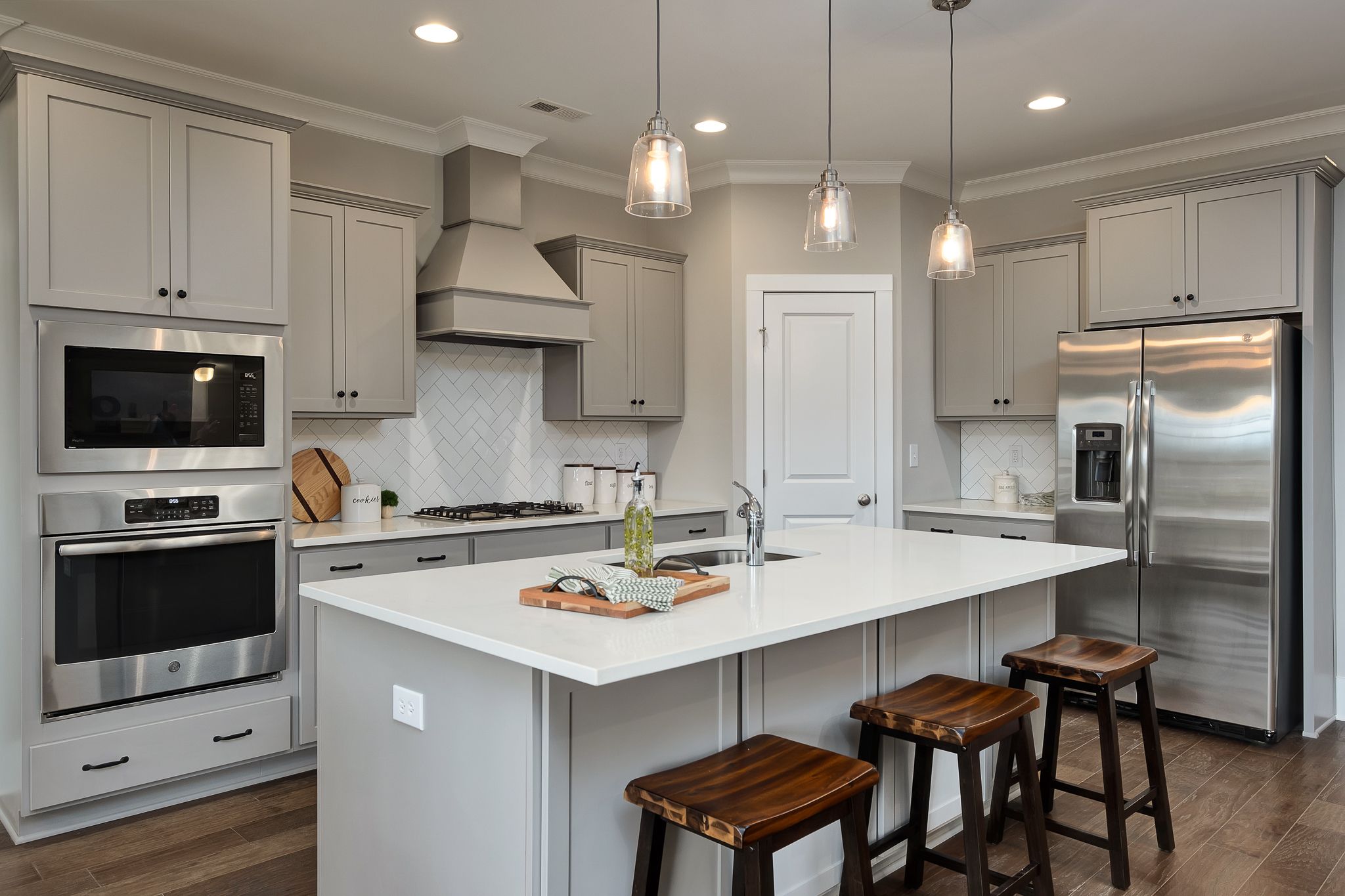 Modern kitchen in Chimney Creek Hampton Cove AL home with gray cabinets white island stainless steel appliances subway tile backsplash