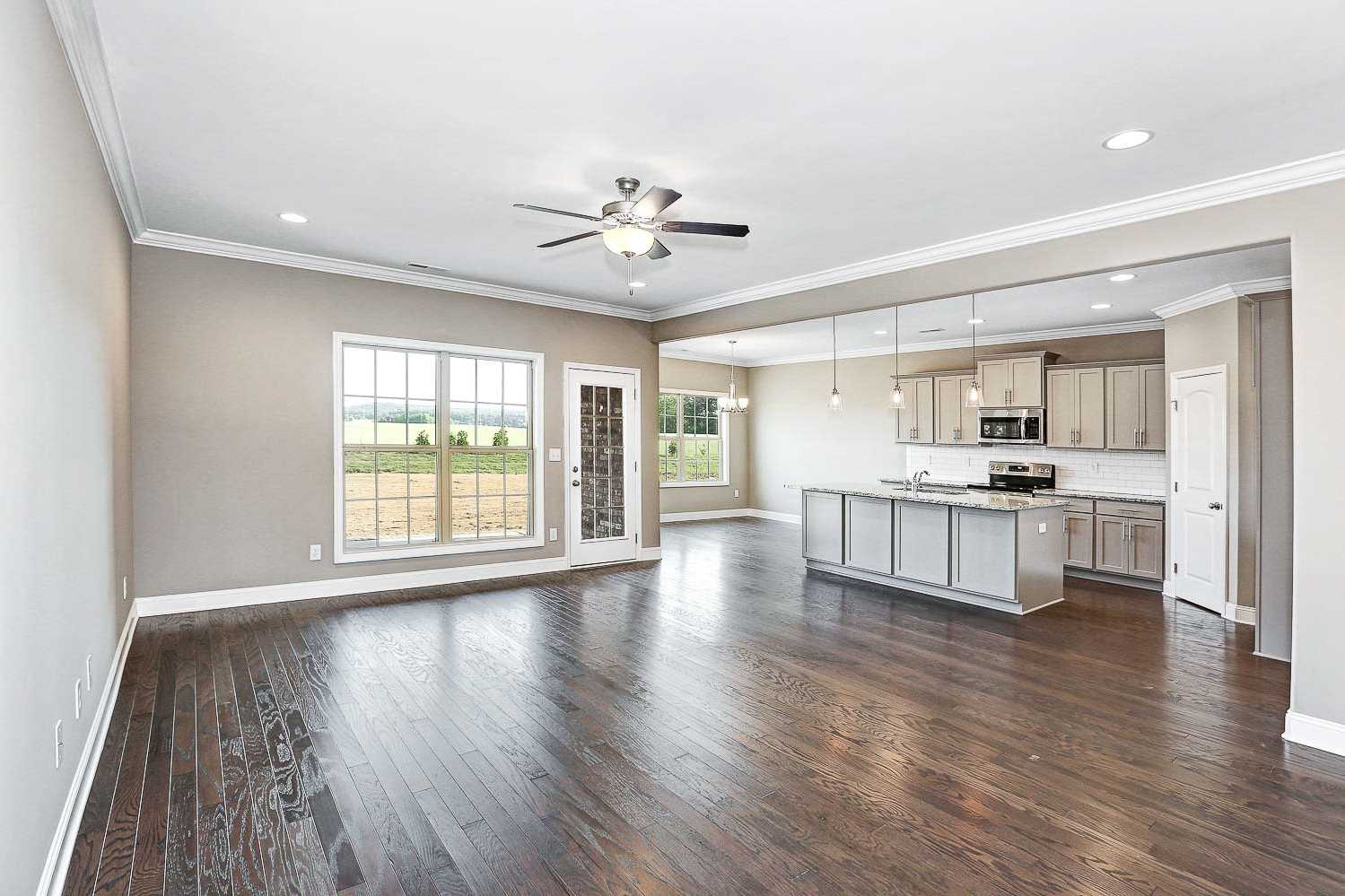 Open-concept kitchen and living area in The Montgomery home design featuring gray island, hardwood floors, ceiling fan, and large field-view windows