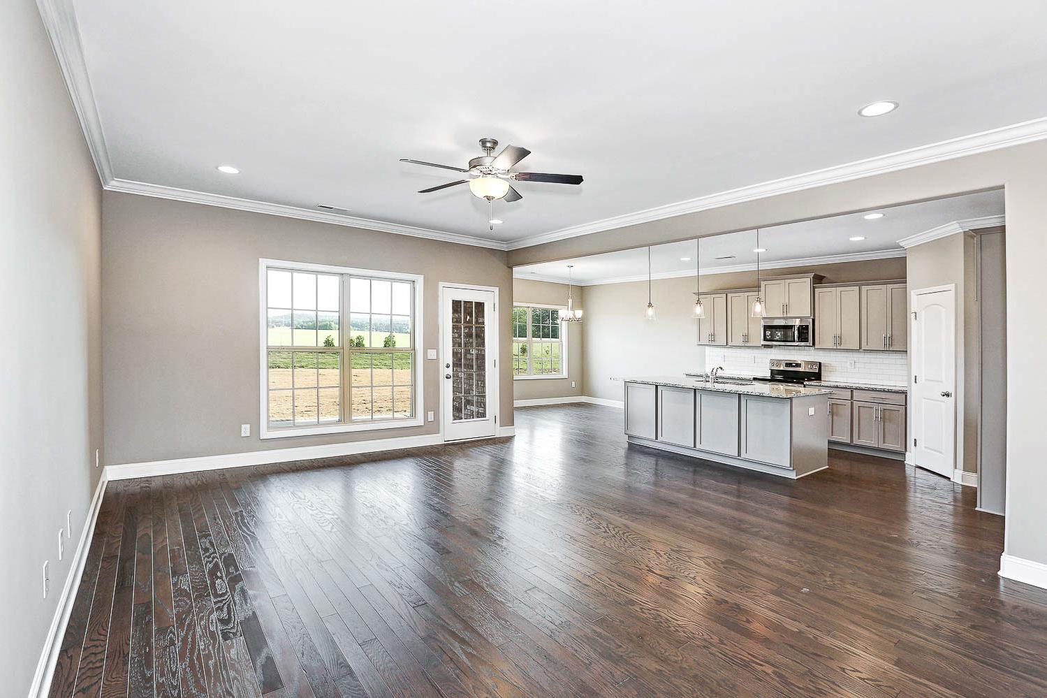 Open-concept kitchen and living area in The Montgomery home design featuring gray island, hardwood floors, ceiling fan, and large field-view windows