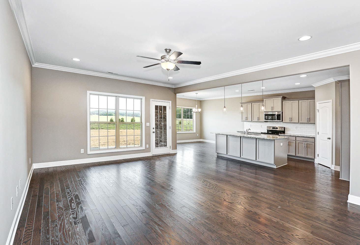 Open-concept kitchen and living area in The Montgomery home design featuring gray island, hardwood floors, ceiling fan, and large field-view windows