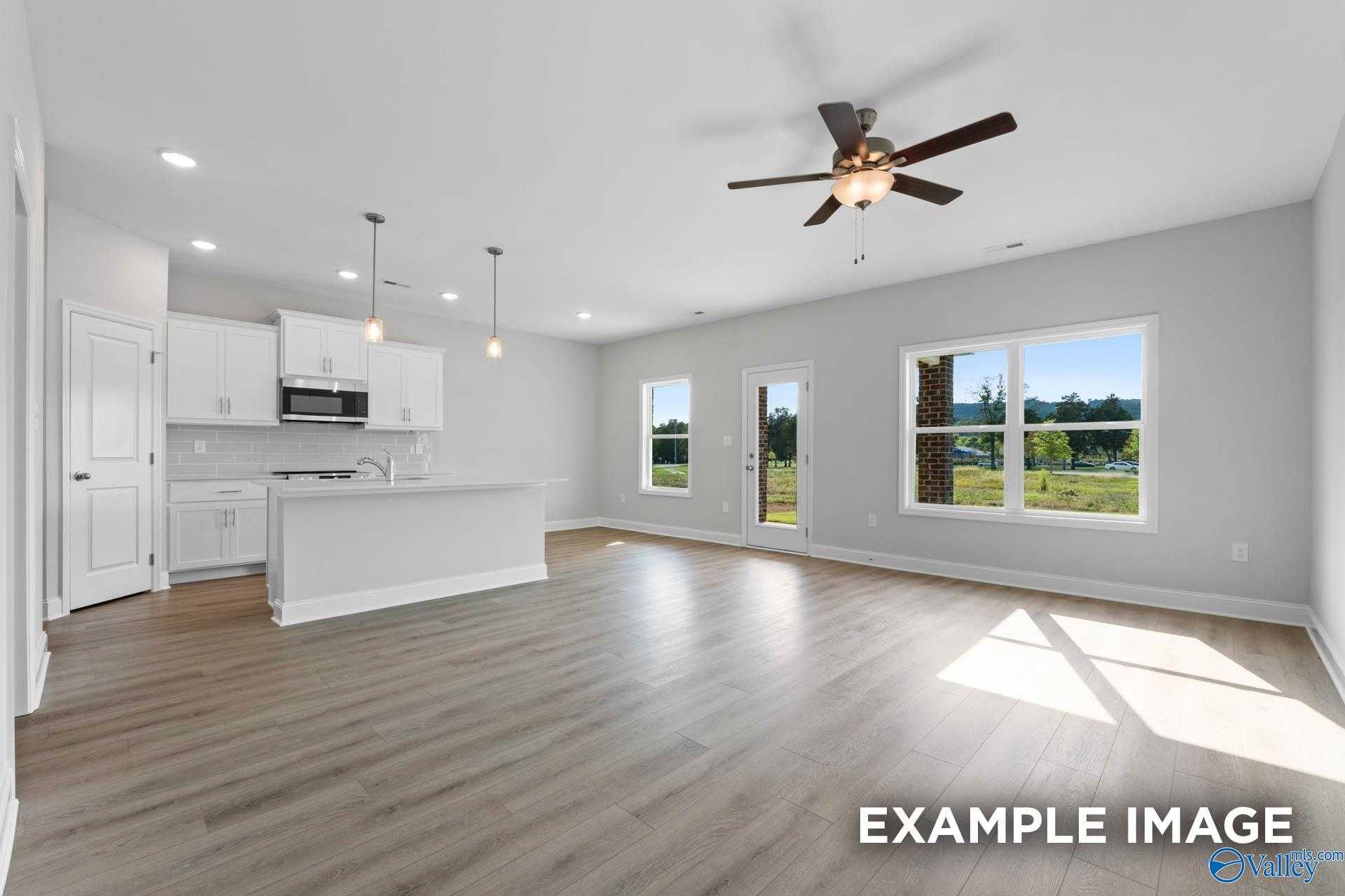 Open-concept kitchen and living area with white cabinets, island, ceiling fan, and backyard views in Davidson Homes The Butler, Huntsville AL