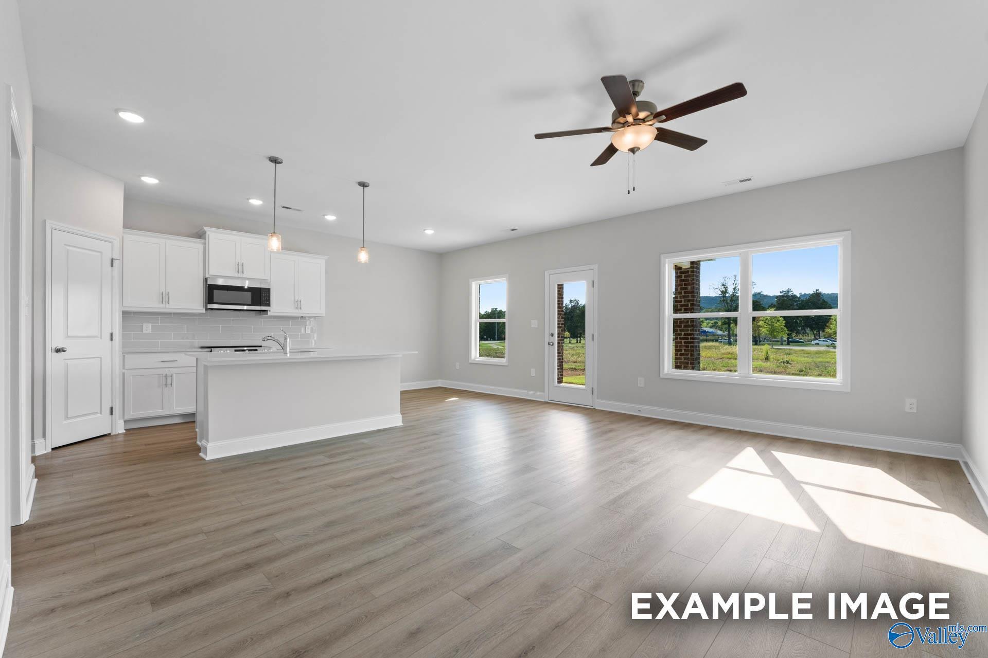 Open-concept kitchen with white cabinets, island, and stainless appliances flowing into living room with ceiling fan and backyard views in Davidson Homes The Butler, Owens Cross Roads, AL