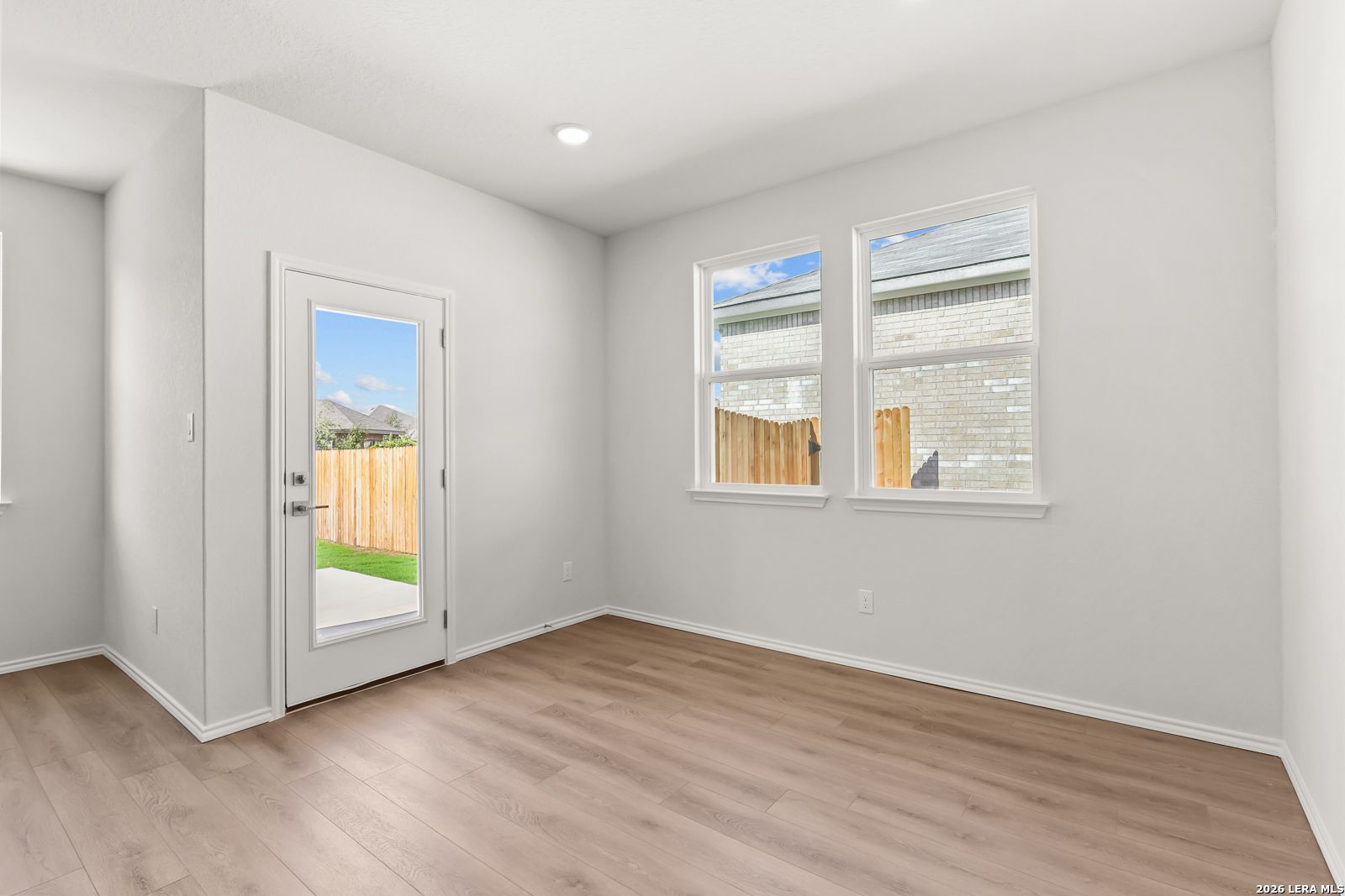 Bright dining area with wood-look flooring, glass back door, and fenced backyard views in Davidson Homes' Daphne I, San Antonio