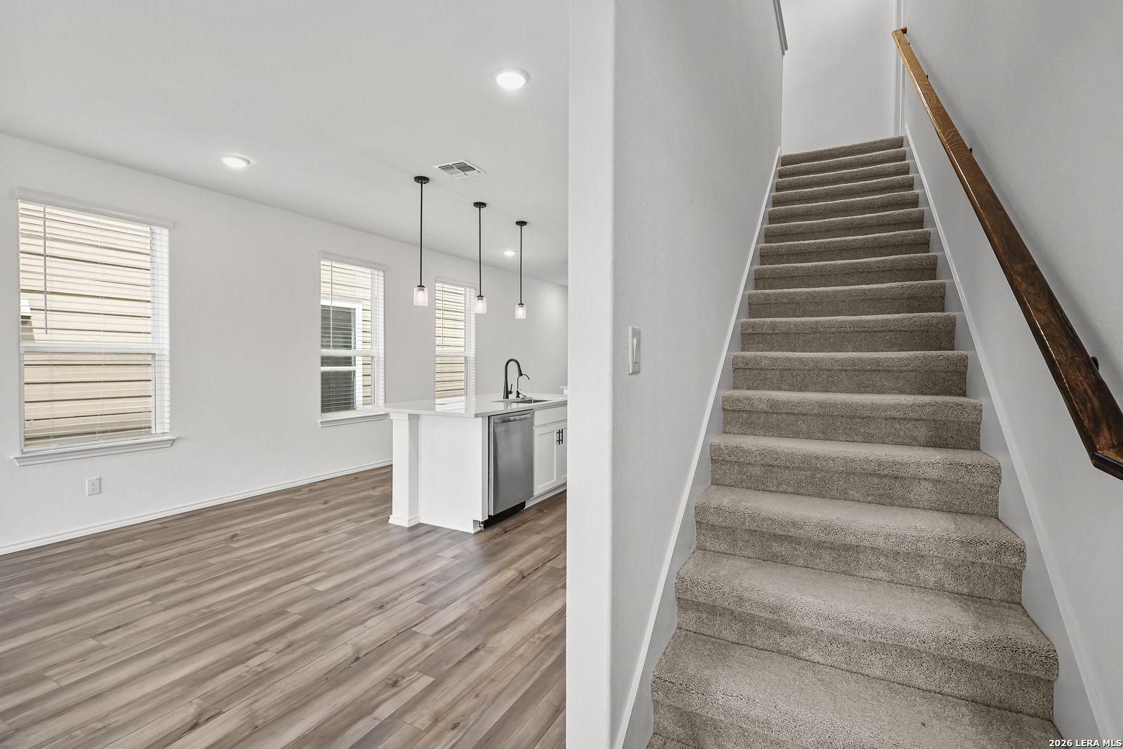 Open-concept kitchen with island and carpeted stairs in The Gillian C floor plan at Meadows at Oak Creek, San Antonio.