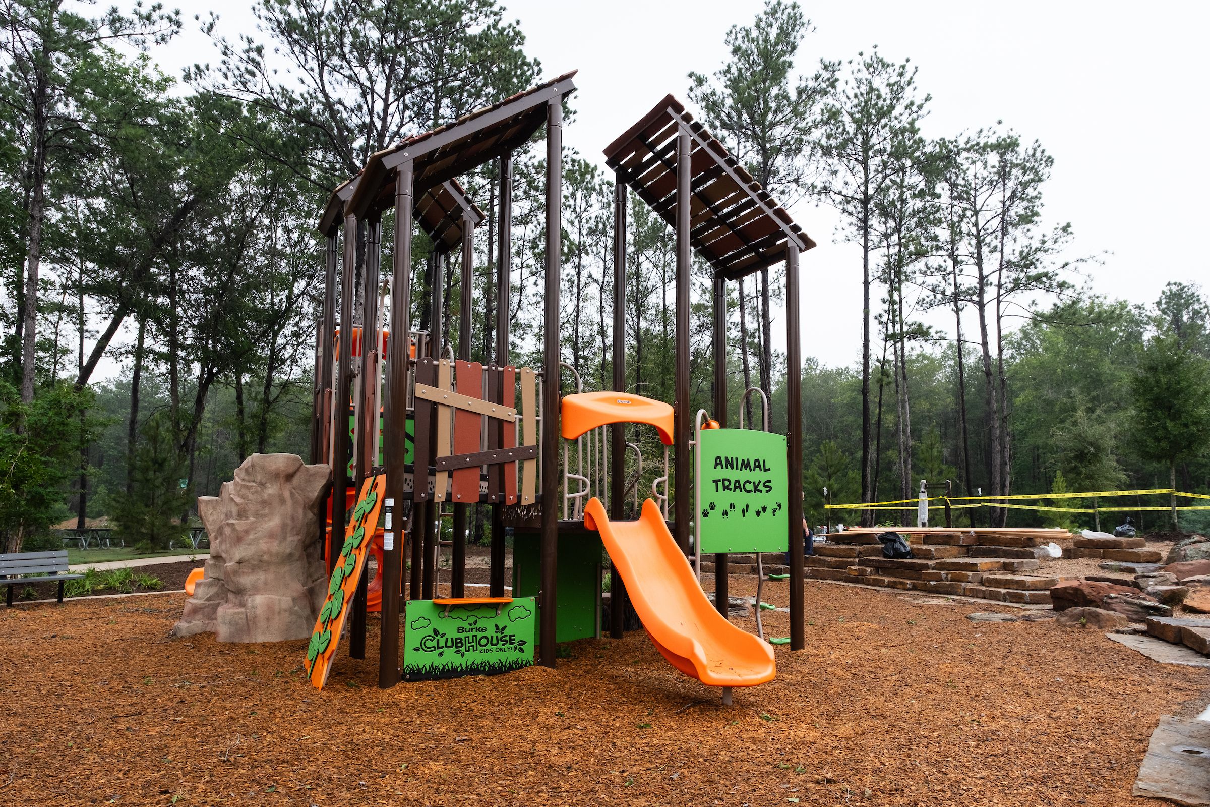 Children's playground with orange slide, animal races climbing walls, and wooden structures at Robins Landing in Houston TX amid pines