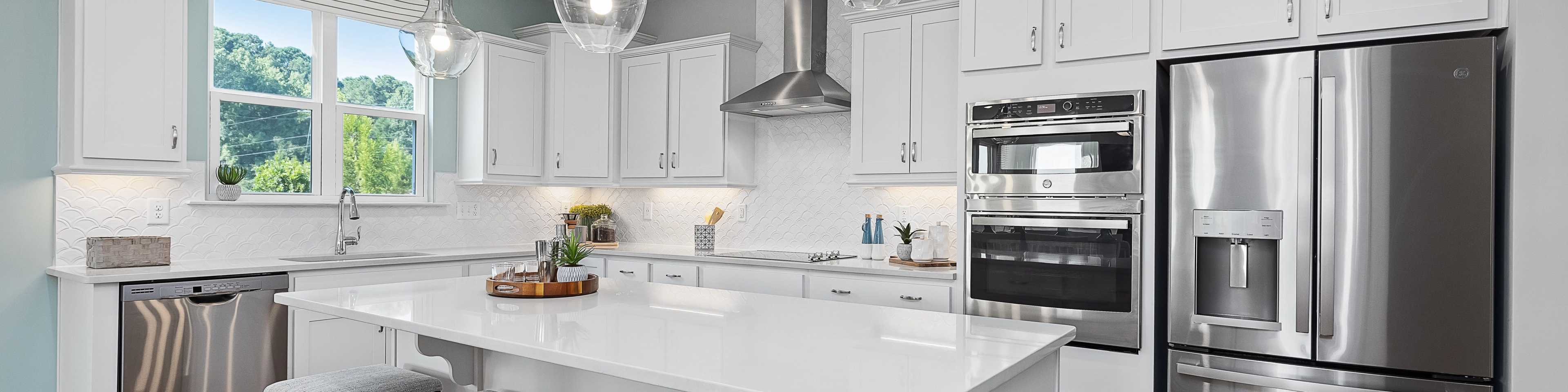 Spacious modern kitchen in Davidson new home with white cabinets, stainless steel appliances, island, and pendant lights