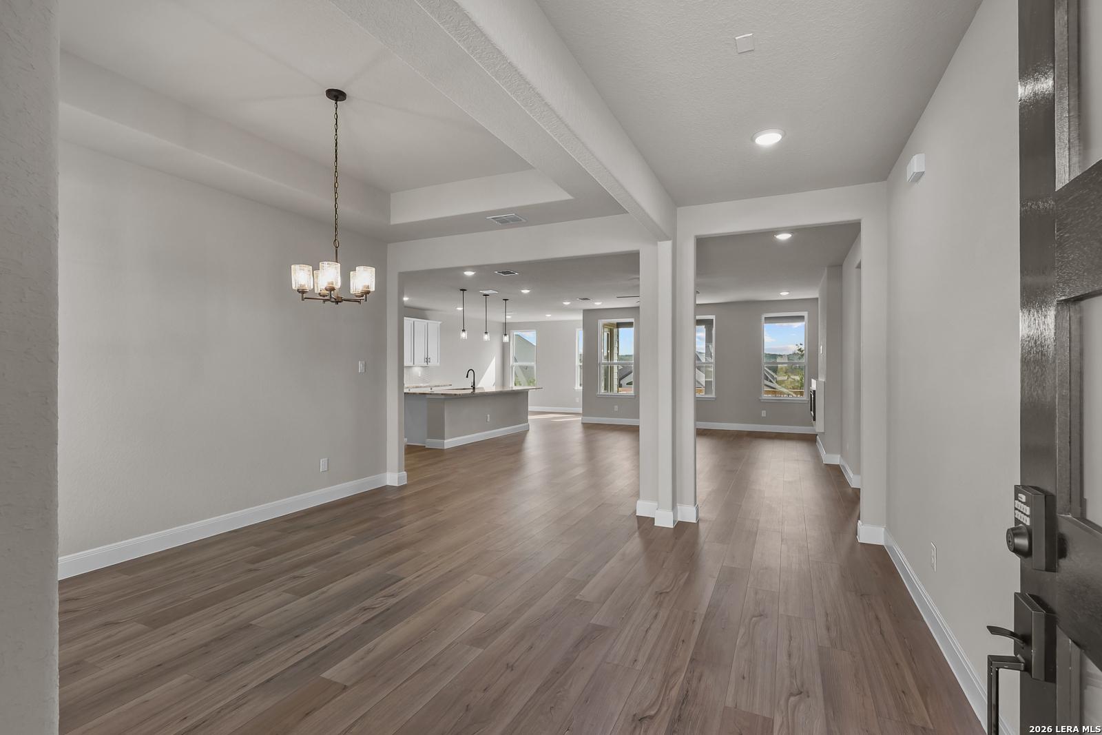 Open-concept living and dining area with wood-look flooring and chandelier in The Foster E floor plan, Potranco Oaks, Castroville, Texas