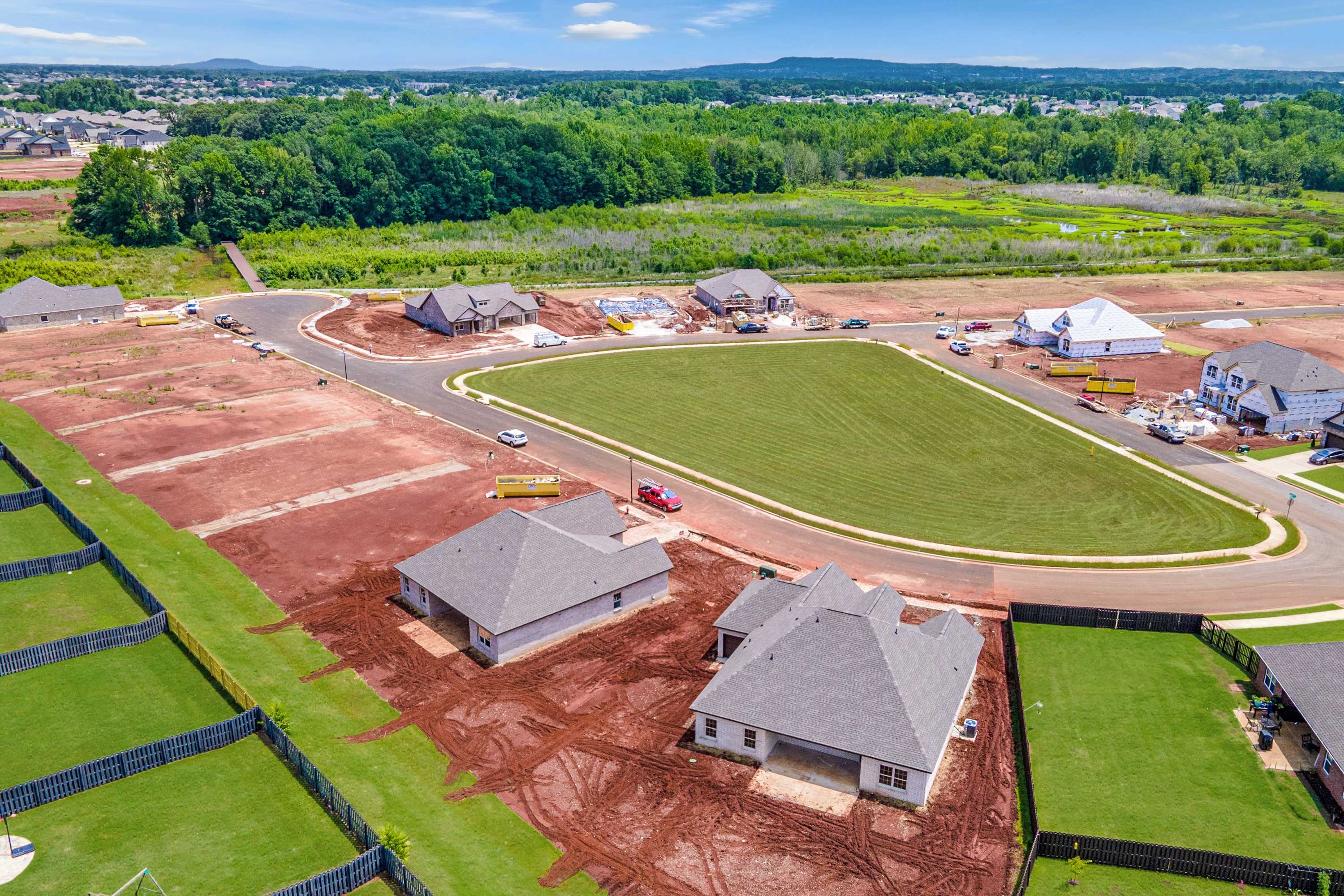 Aerial view of new homes under construction at Barnett's Crossing in Madison, Alabama with green lawns, dirt lots and winding roads