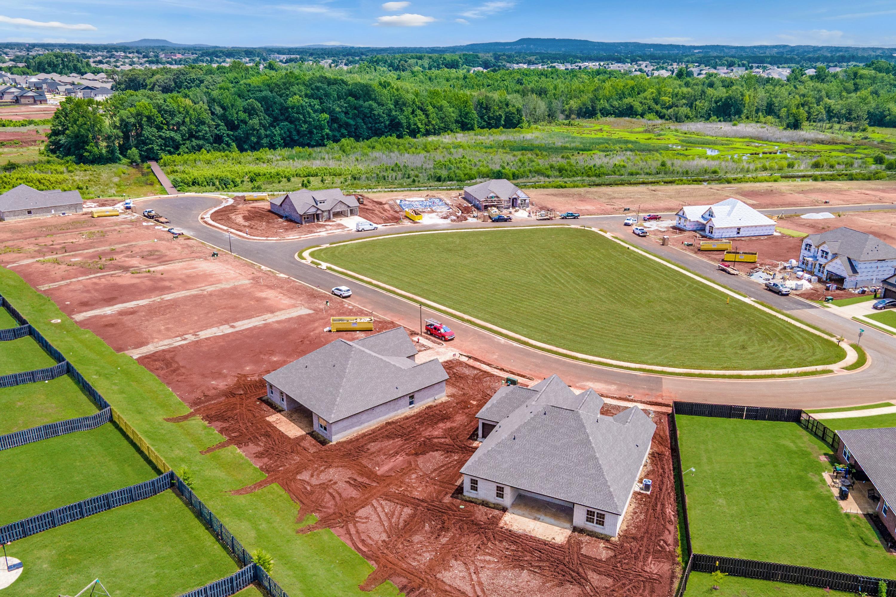 Aerial view of new homes under construction at Barnett's Crossing in Madison, Alabama with green lawns, dirt lots and winding roads