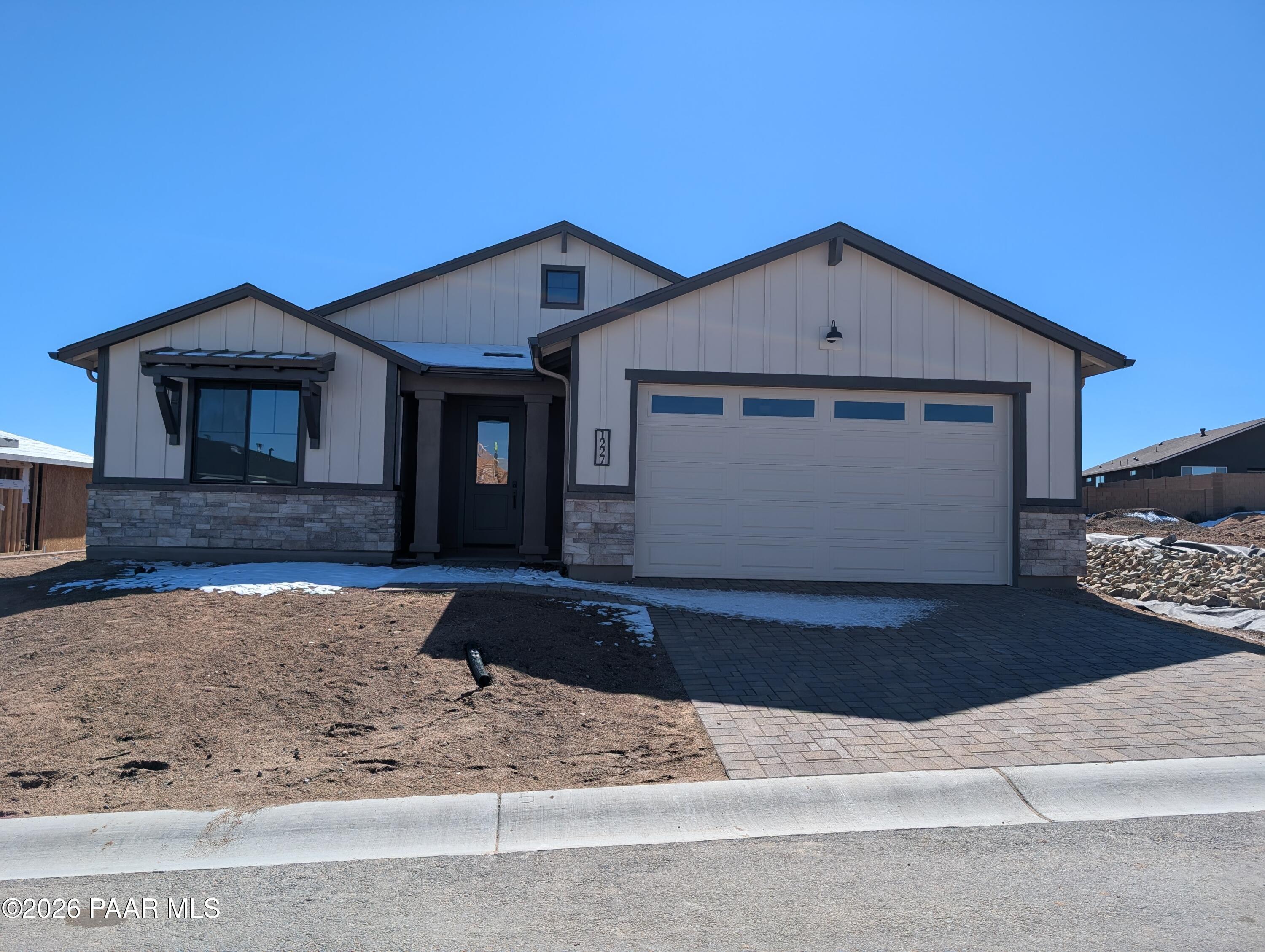 Modern single-story home with 3-car garage, beige siding, stone accents, and snowy front yard in Prescott, Arizona - Davidson Homes Sheridan II G