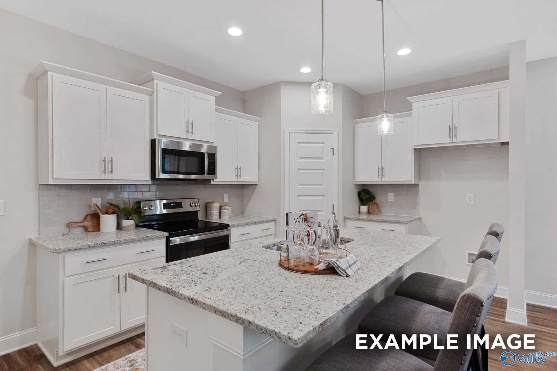 White shaker kitchen with granite island, stainless appliances, and pendant lighting in The Camilla C plan, Hartselle, Alabama