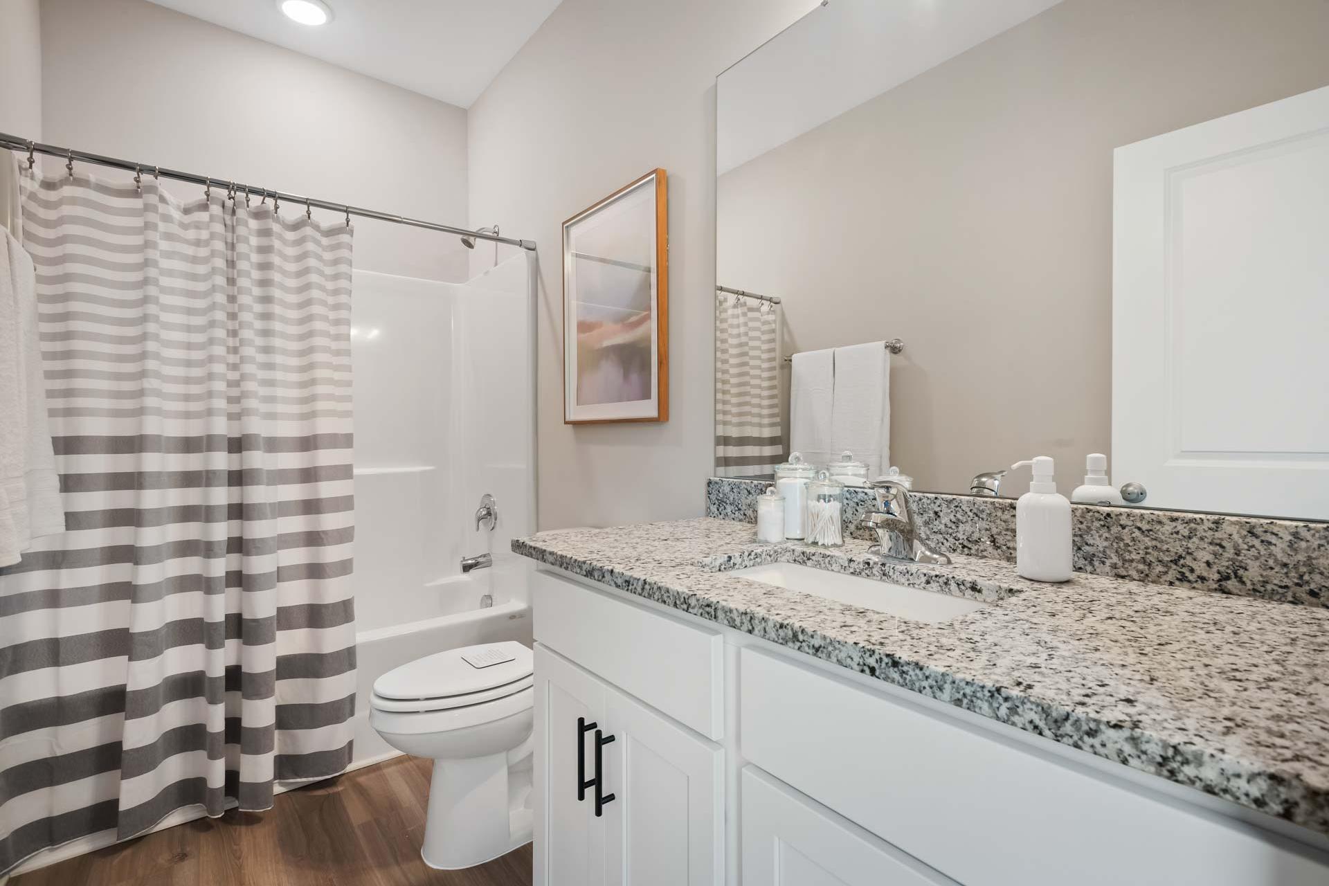 Contemporary bathroom at Durham Farms in Harvest AL featuring walk-in shower with striped curtain, granite vanity, and hardwood floors