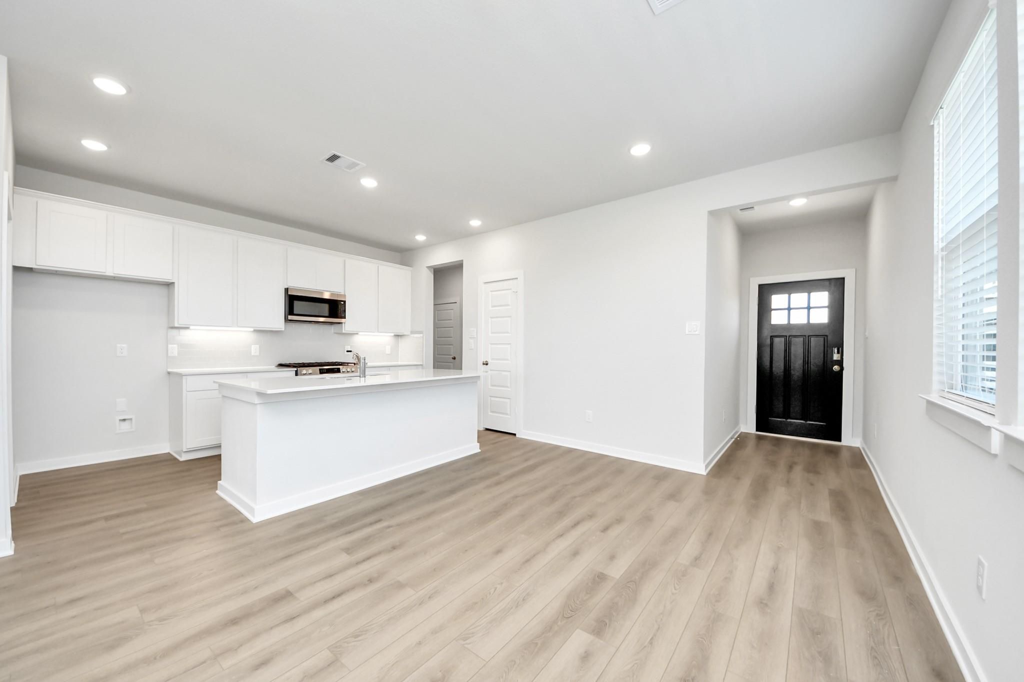 Open-concept kitchen with white shaker cabinets, center island, and luxury vinyl plank flooring in Davidson Homes Costa A plan, Beasley TX