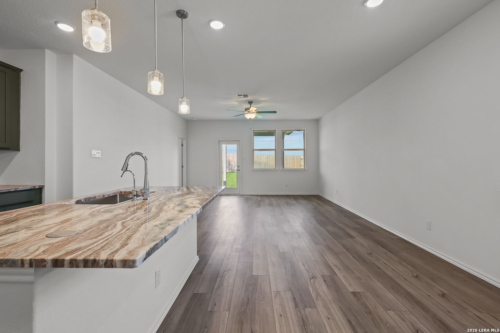 Open-concept kitchen and living area with stone island countertop in The Brazos B floor plan at Agave, San Antonio, Texas.