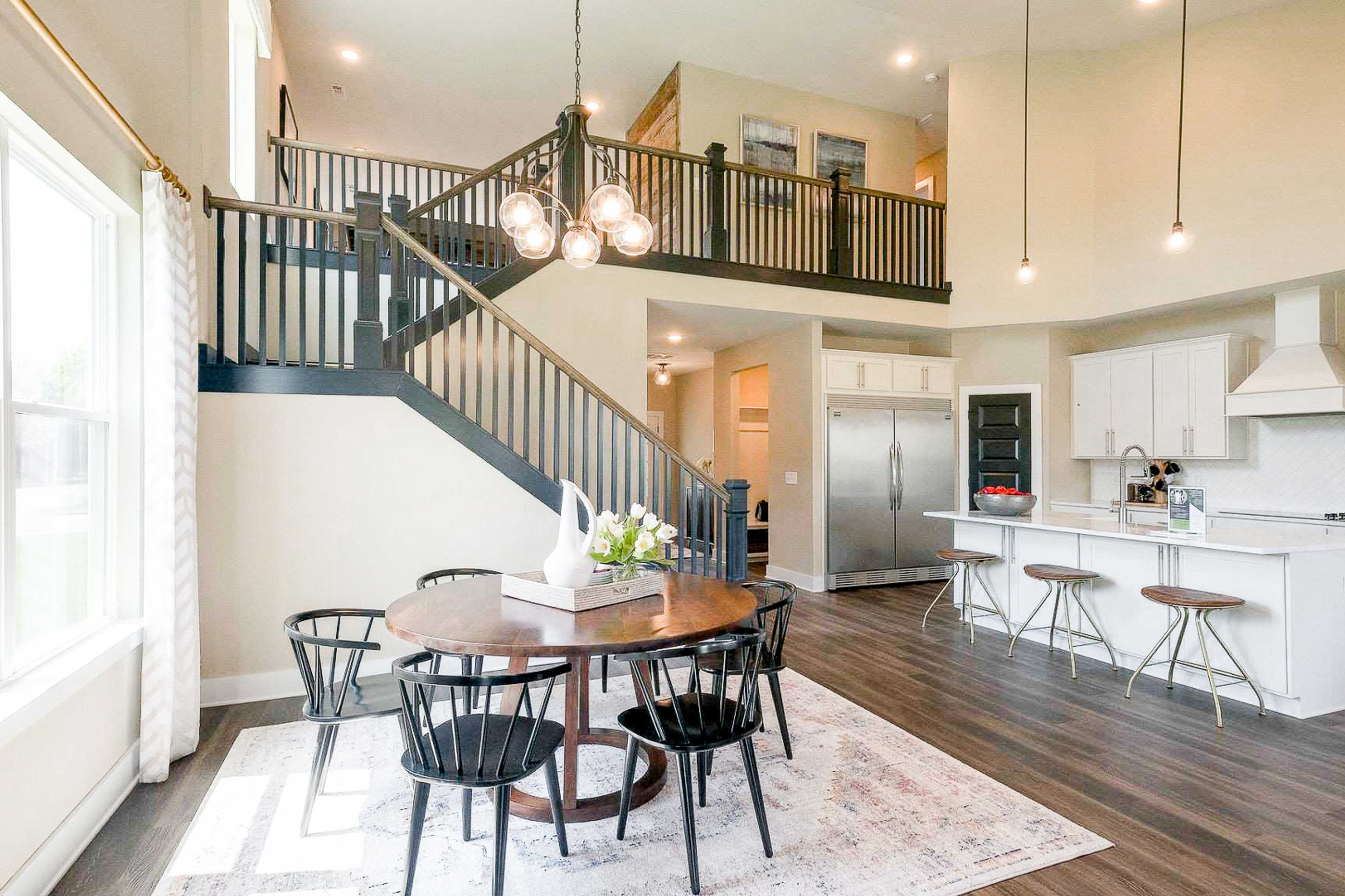 Open-concept kitchen and dining area at The Meadows in Smyrna, TN by Davidson Homes with white cabinets, hardwood floors, and staircase