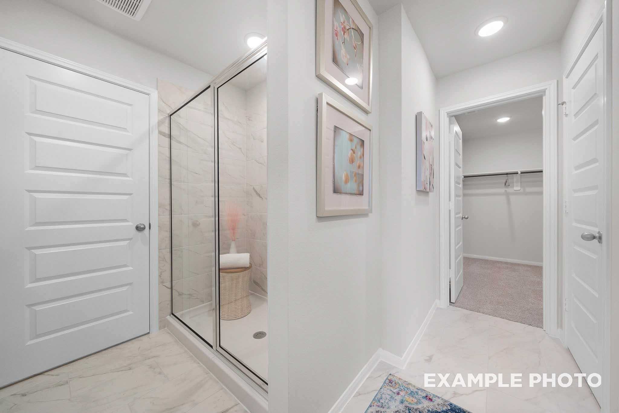 Master bathroom in The Trinity E showcasing frameless glass shower, tiled floor, and adjacent walk-in closet with built-in storage