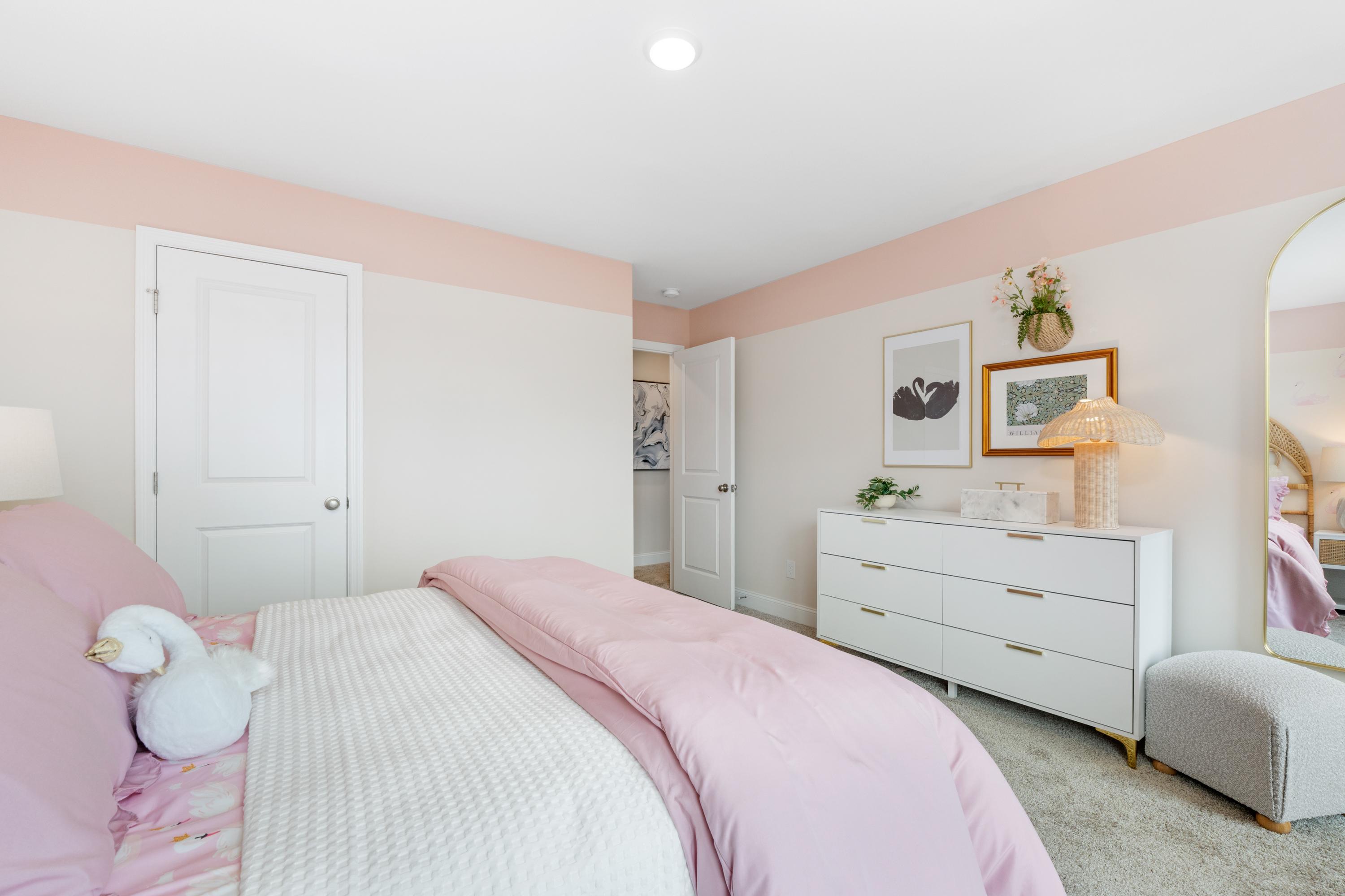 Cozy girl's bedroom in Pavilion Huntsville AL by Davidson Homes with pink bedding, white dresser, and arched mirror