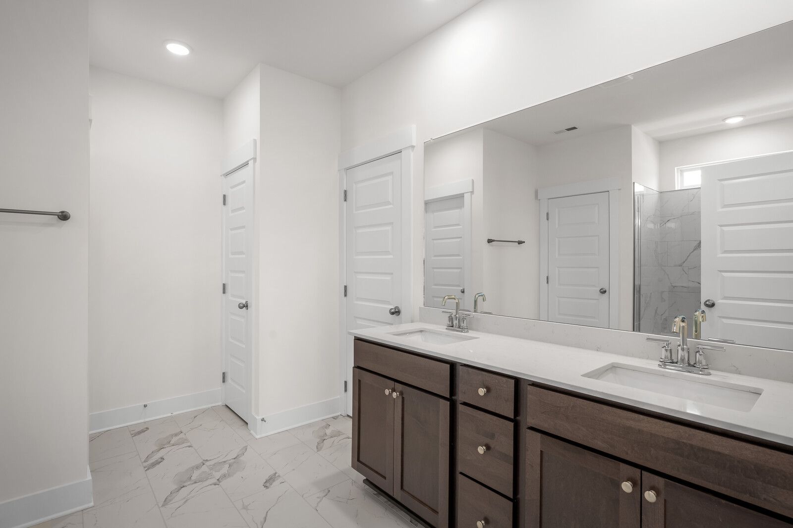 Modern master bathroom in The Cottonwood featuring a double vanity with stone countertops and marble-style tile flooring.