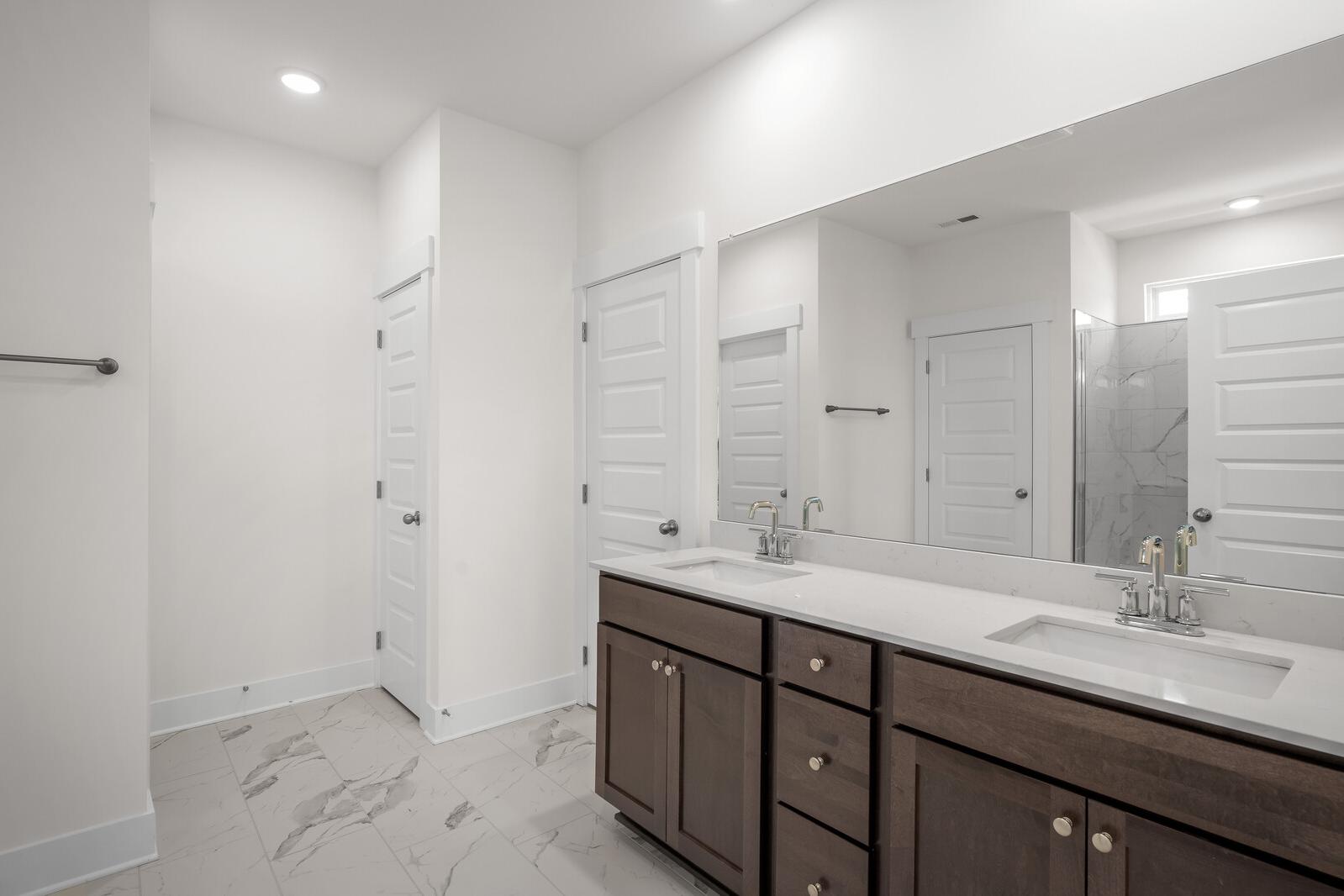 Modern master bathroom in The Cottonwood featuring a double vanity with stone countertops and marble-style tile flooring.
