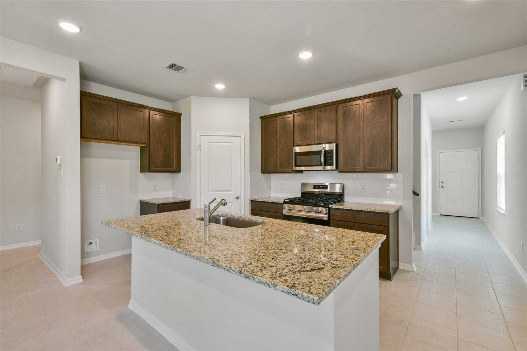 Open-concept kitchen with dark wood cabinets, granite island sink, stainless microwave and stove in Davidson Homes Sabine E, Dayton, Texas