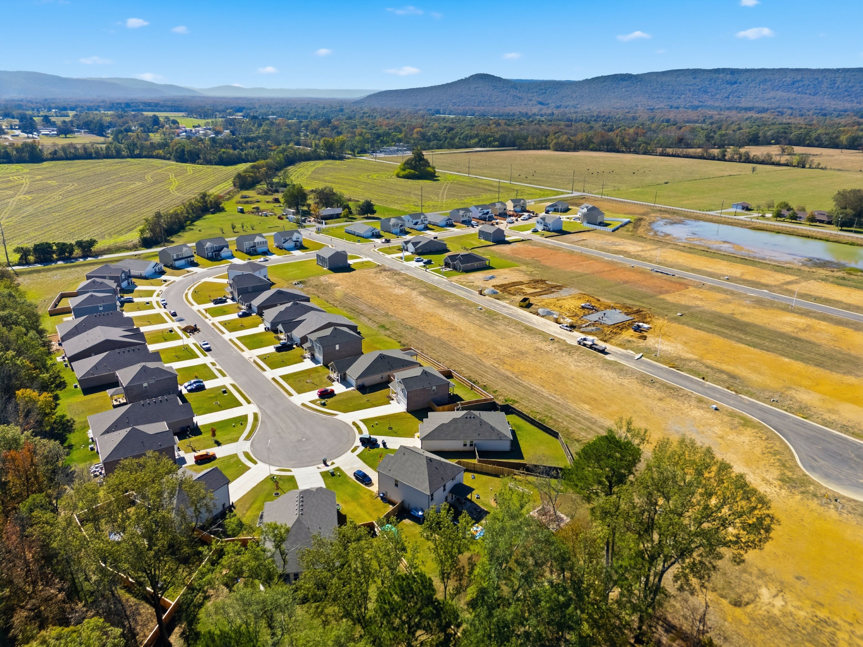 Aerial view of Ramsay Cove new homes in Owens Cross Roads Alabama with construction sites, pond, and surrounding farmland mountains