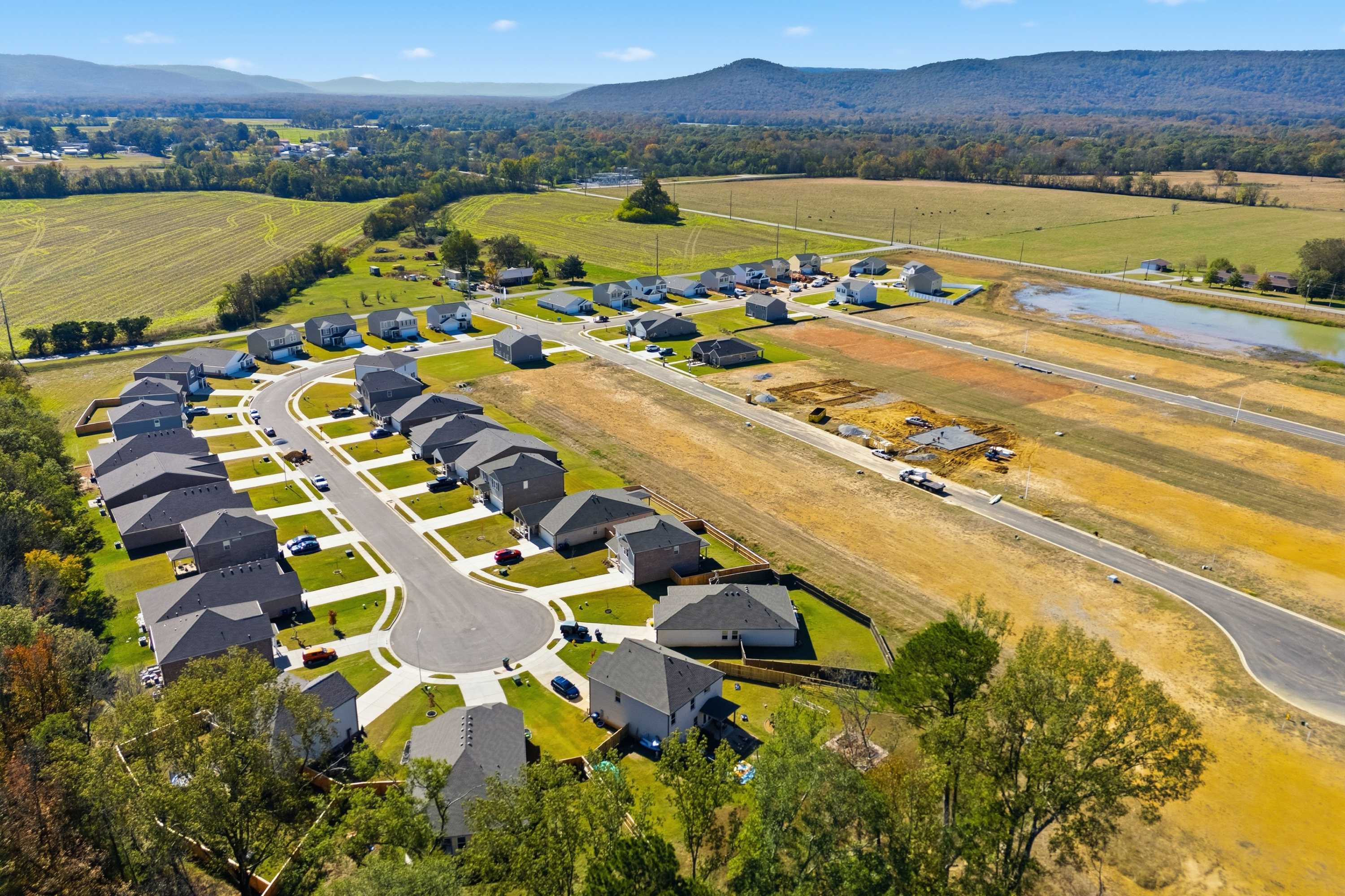 Aerial view of Ramsay Cove new homes in Owens Cross Roads Alabama with construction sites, pond, and surrounding farmland mountains