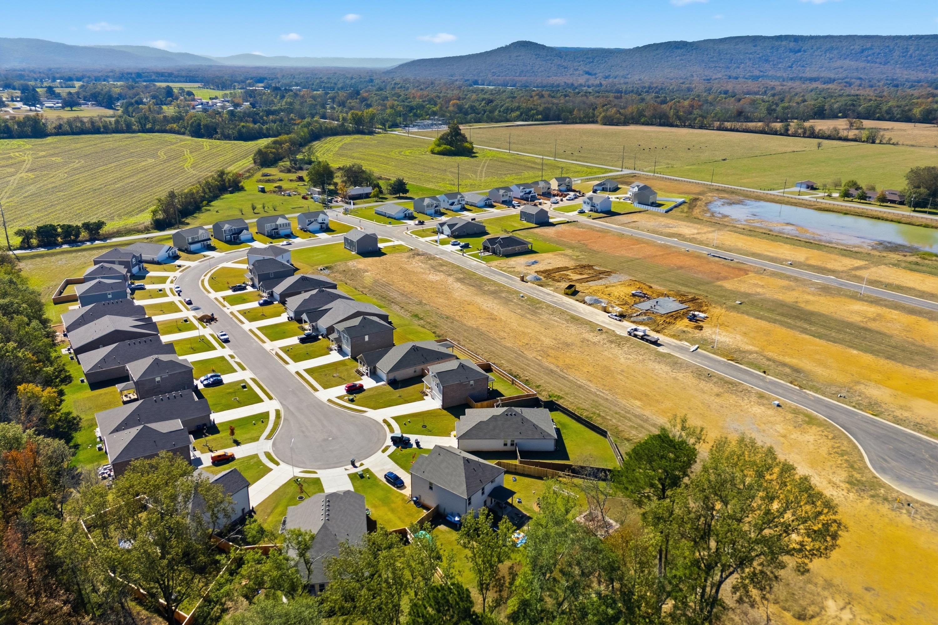 Aerial view of Ramsay Cove new homes in Owens Cross Roads Alabama with construction sites, pond, and surrounding farmland mountains
