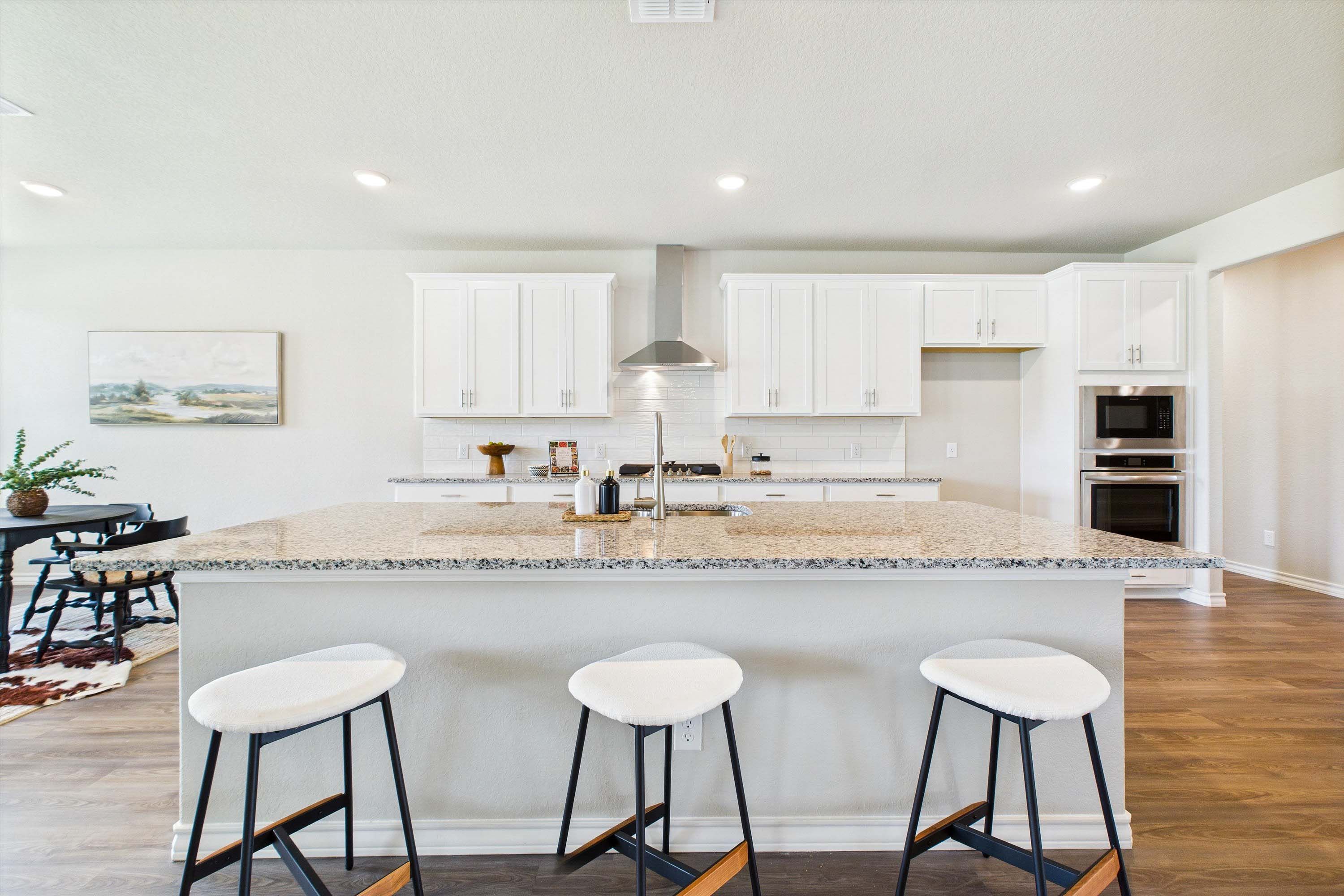 Modern kitchen in The Foster with a large granite island, white cabinetry, stainless steel appliances, and breakfast nook.
