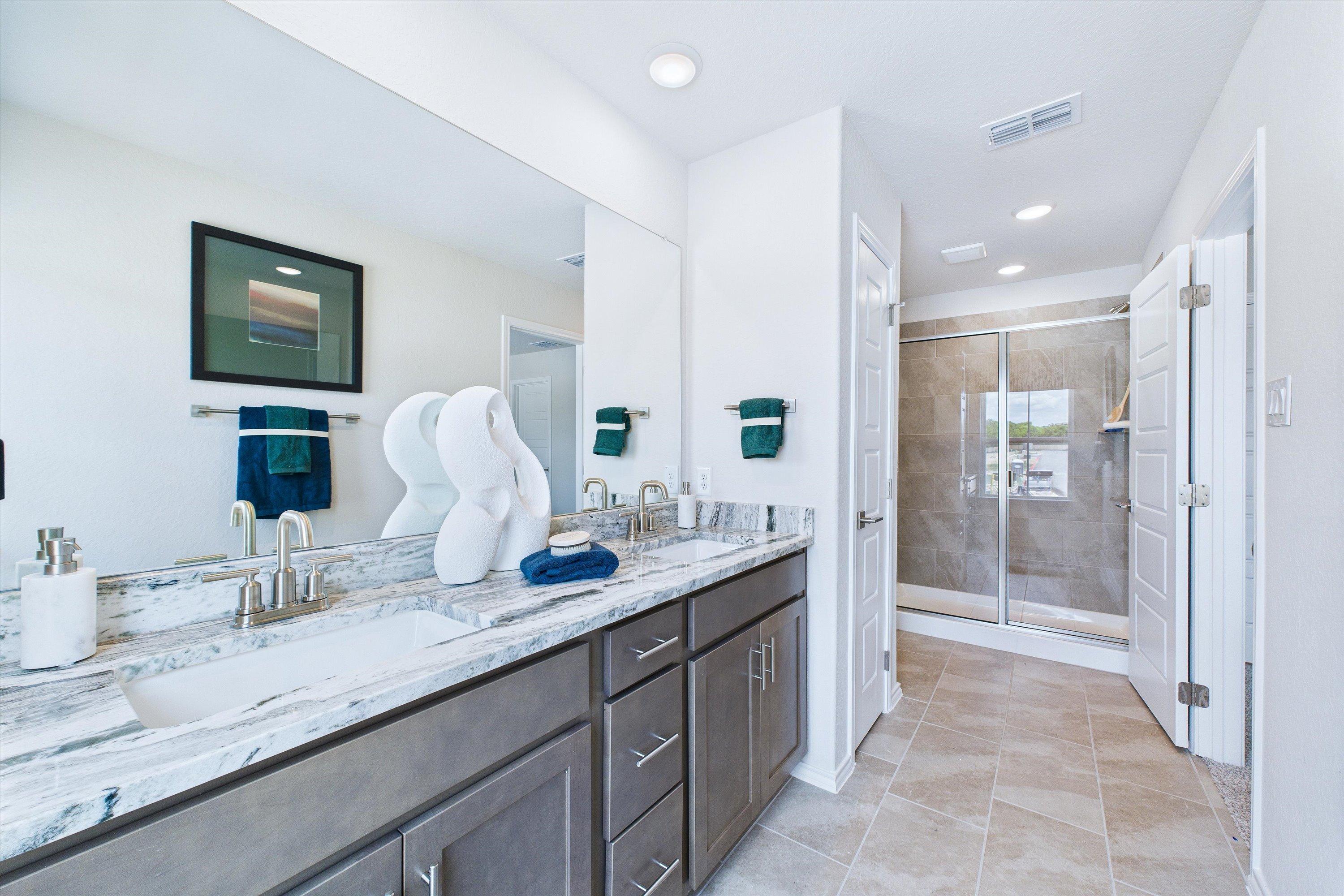 Spacious primary bathroom in Cedar Heights San Antonio with double vanity, quartz counters, gray cabinets, and frameless shower