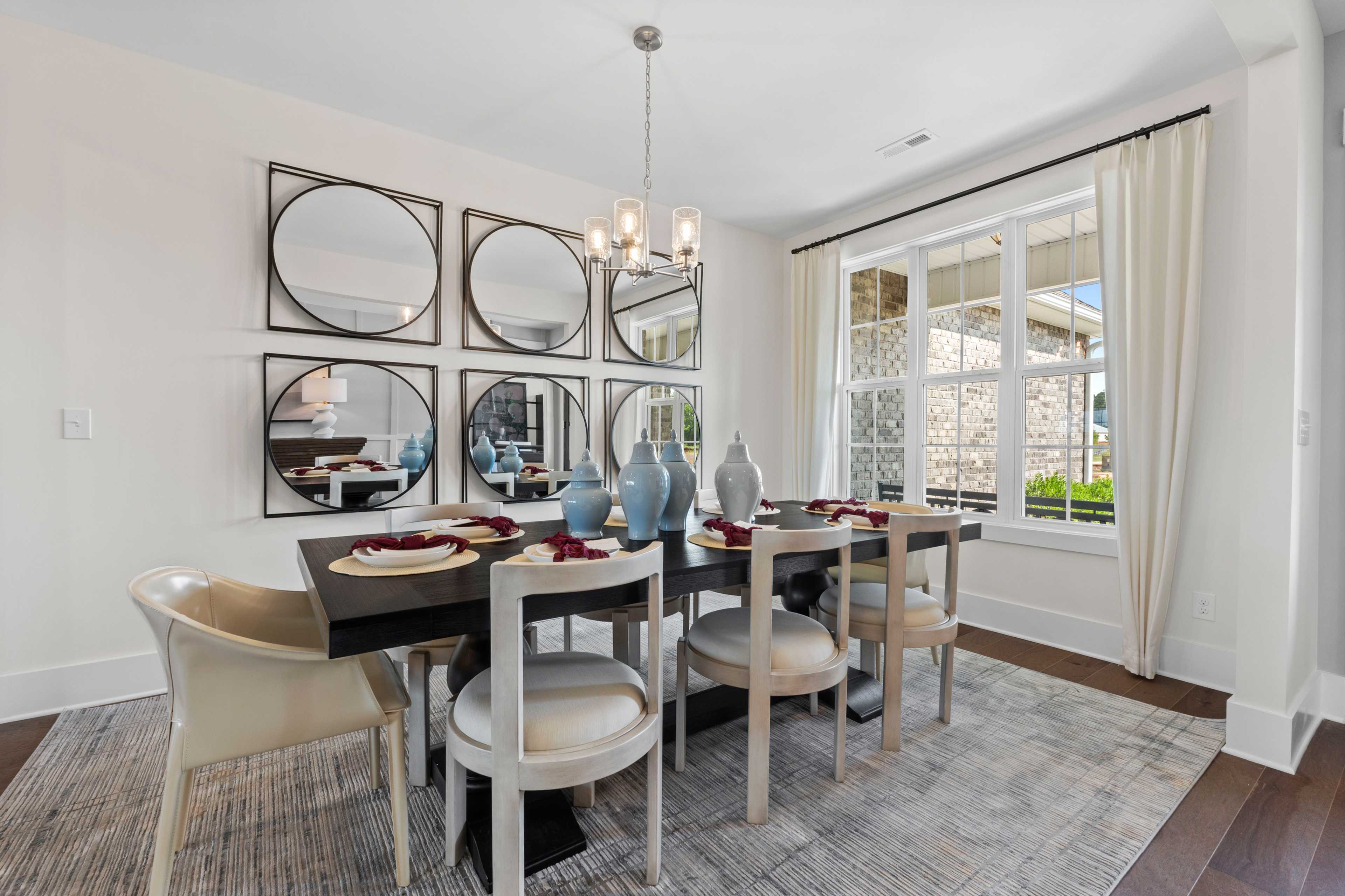 Elegant dining room in Creekside Harvest Alabama with dark wood table, upholstered chairs, mirror wall, chandelier, and window views