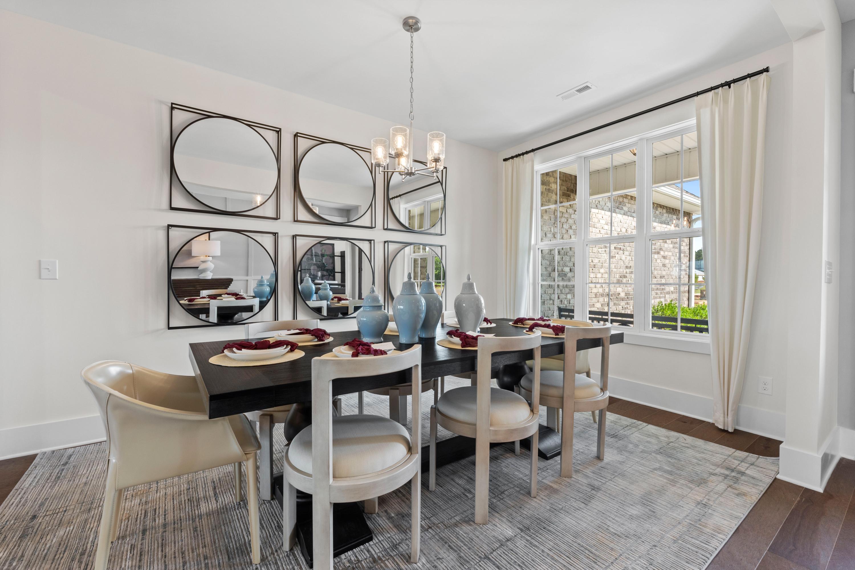 Elegant dining room in Creekside Harvest Alabama with dark wood table, upholstered chairs, mirror wall, chandelier, and window views