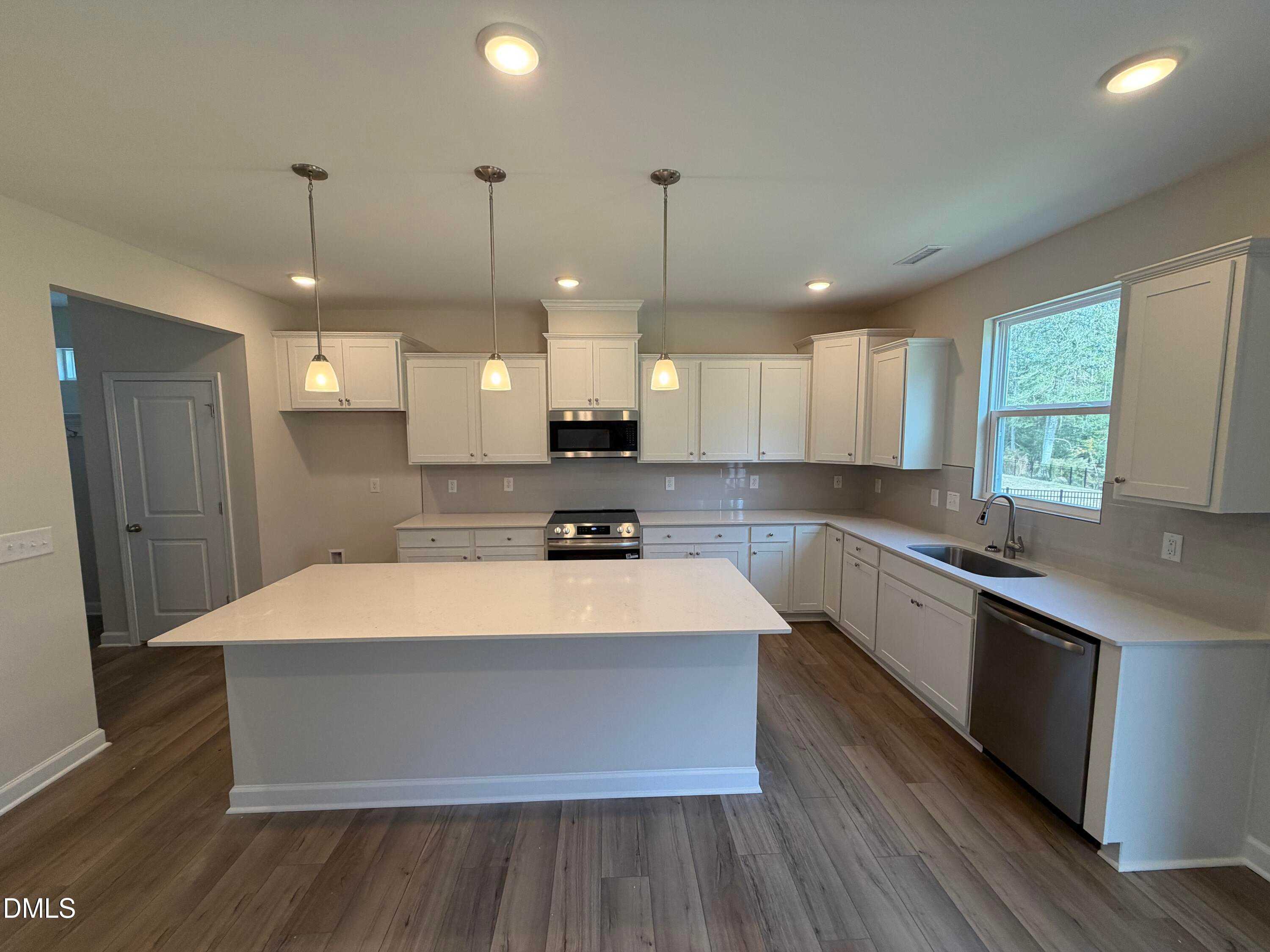 Modern white kitchen with oversized island, stainless steel appliances, and recessed lighting in The Hickory II A by Davidson Homes, Lillington, NC