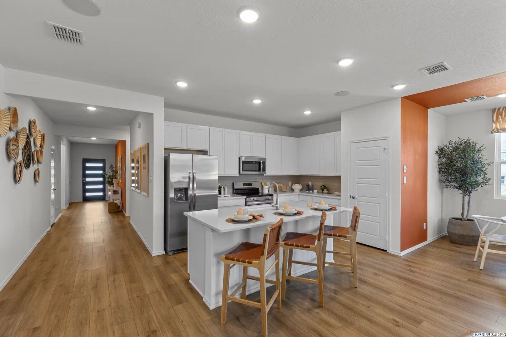 Modern white kitchen with quartz island, stainless appliances, and orange accent wall in Davidson Homes The Daphne K, Bricewood San Antonio