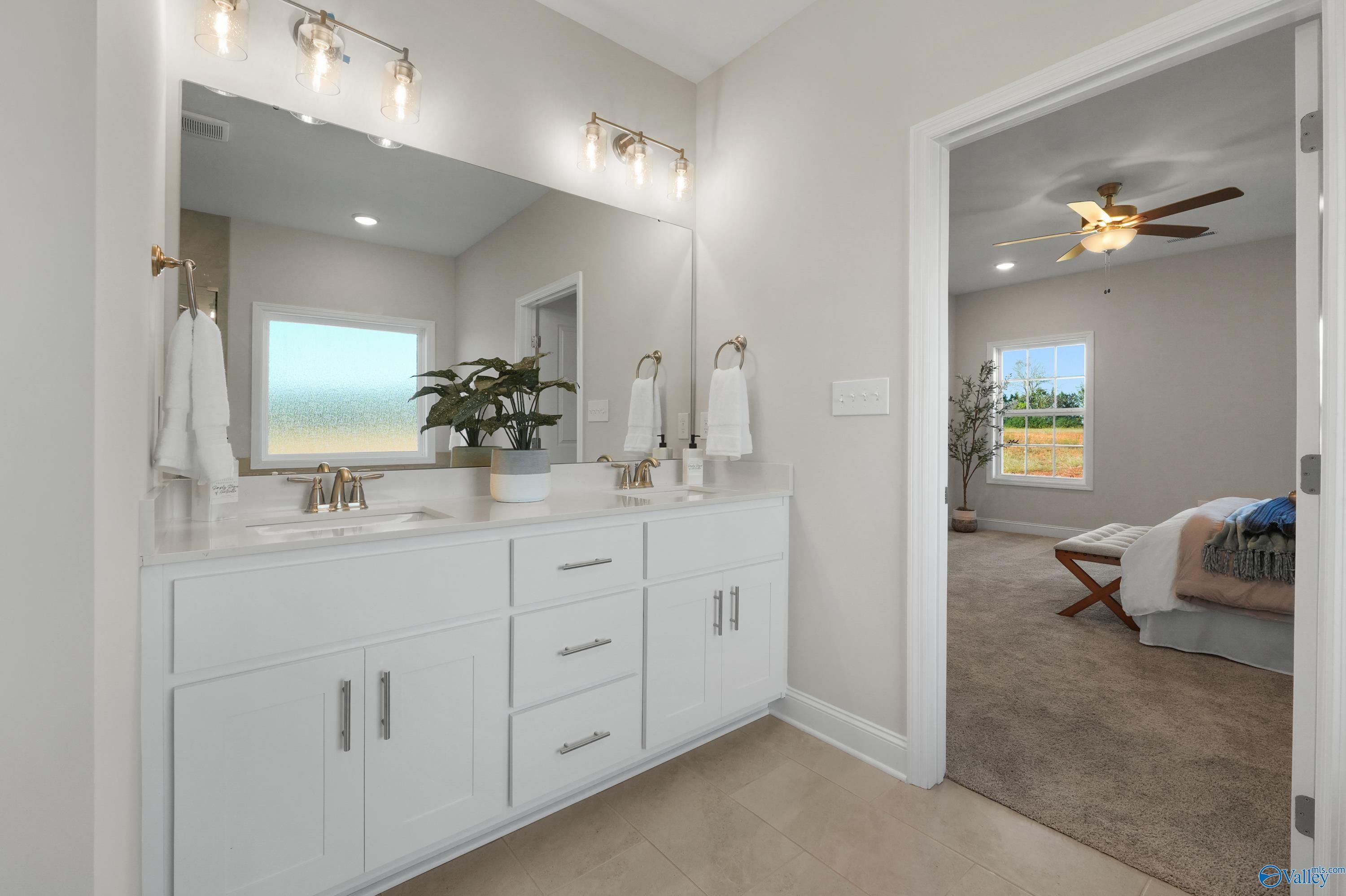 Elegant master bathroom with double vanity, large mirrors, plants, and adjacent bedroom in Davidson Homes The Rockford B, Toney, Alabama