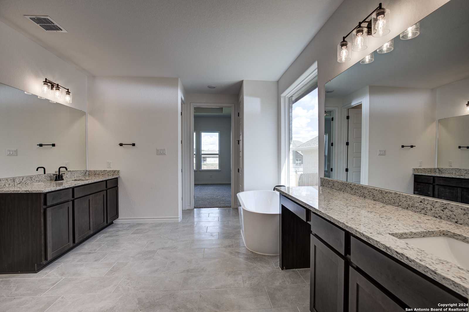 Elegant master bathroom with double dark wood vanity, freestanding tub, and large window in The Garner B, Castroville, Texas