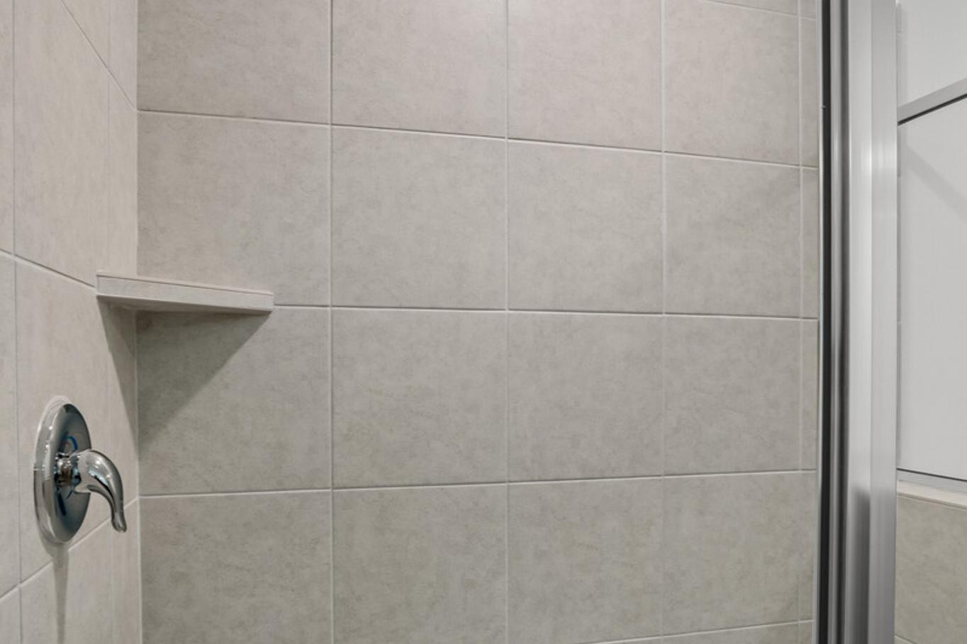 Modern walk-in shower in The Logan C master bathroom with beige subway tiles, frameless glass enclosure, and rainfall showerhead