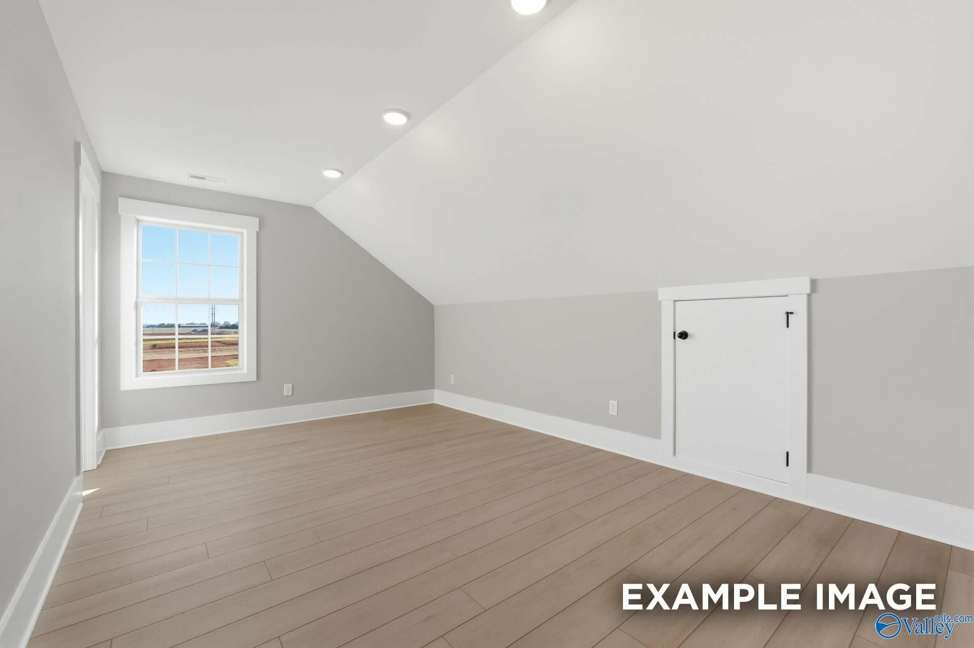 Bright upstairs bedroom featuring sloped gray walls, large window with rural view, hardwood floors in The Emory by Davidson Homes, Decatur AL