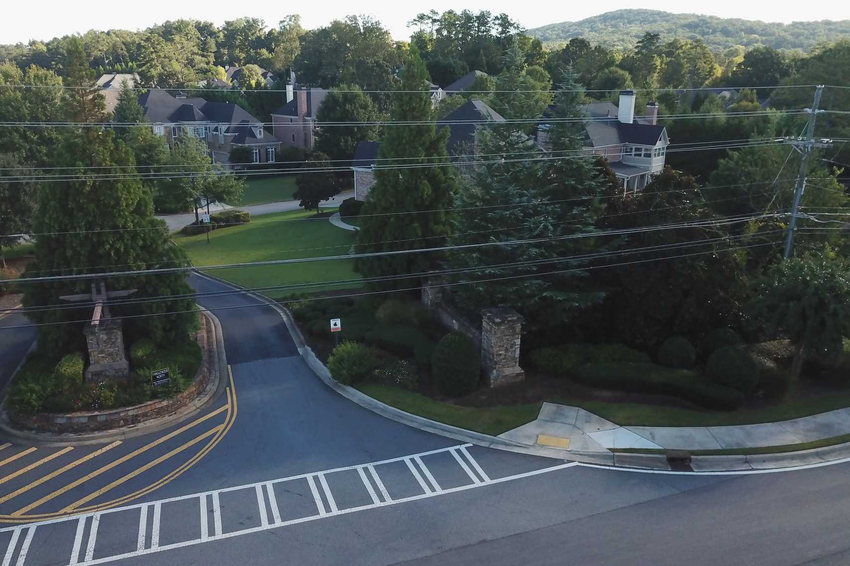 Welcoming stone entrance at Tanglewood in East Cobb, Georgia with curved driveway, lush greenery and wooded hills