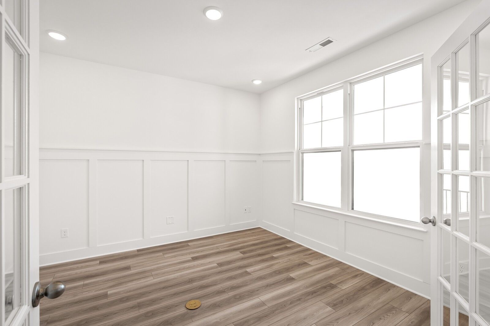 Bright interior room with white wainscoting walls, French doors, large windows, recessed lights, and light wood floors in Davidson Homes The Ash C, Mt. Juliet