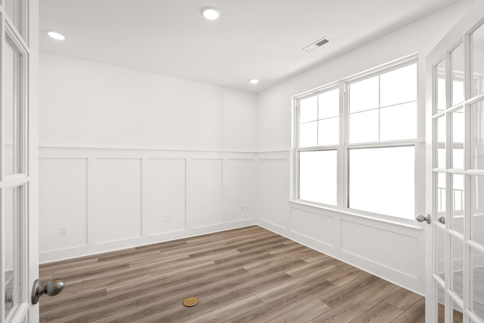 Bright interior room with white wainscoting walls, French doors, large windows, recessed lights, and light wood floors in Davidson Homes The Ash C, Mt. Juliet