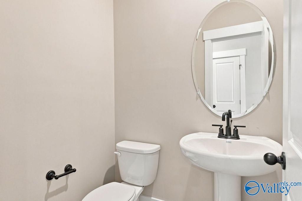 Half-bath with pedestal sink and oval mirror in The Rockford floor plan by Davidson Homes in Cain Park, Hartselle, Alabama.