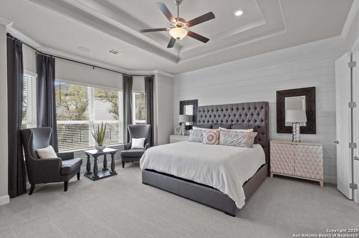 Elegant master bedroom with tufted gray headboard, king bed, armchairs, and ceiling fan in Davidson Homes The Garner B, San Antonio