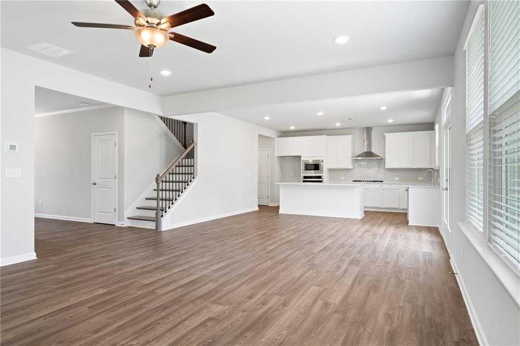 Open-concept kitchen and living space with white cabinets, island, hardwood floors, and staircase in Davidson Homes The Hickory B, Winder, GA