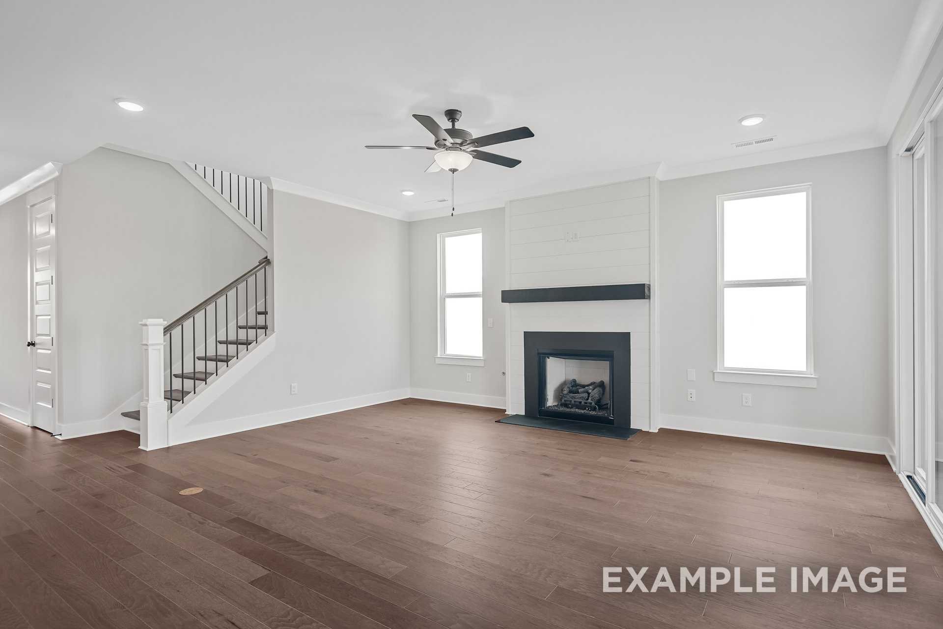 Spacious great room in The Hathaway featuring modern fireplace, hardwood floors, ceiling fan, and open staircase