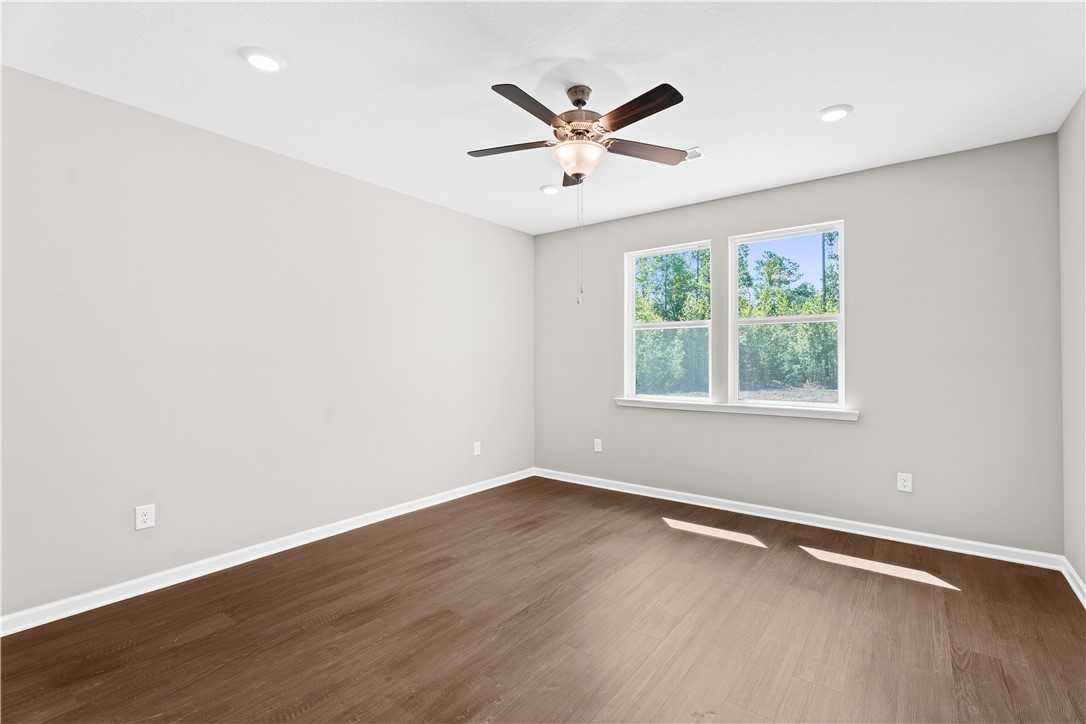 Spacious secondary bedroom with hardwood floors, ceiling fan, and large windows overlooking trees in Evermore Homes The Orion, Cusseta, Alabama