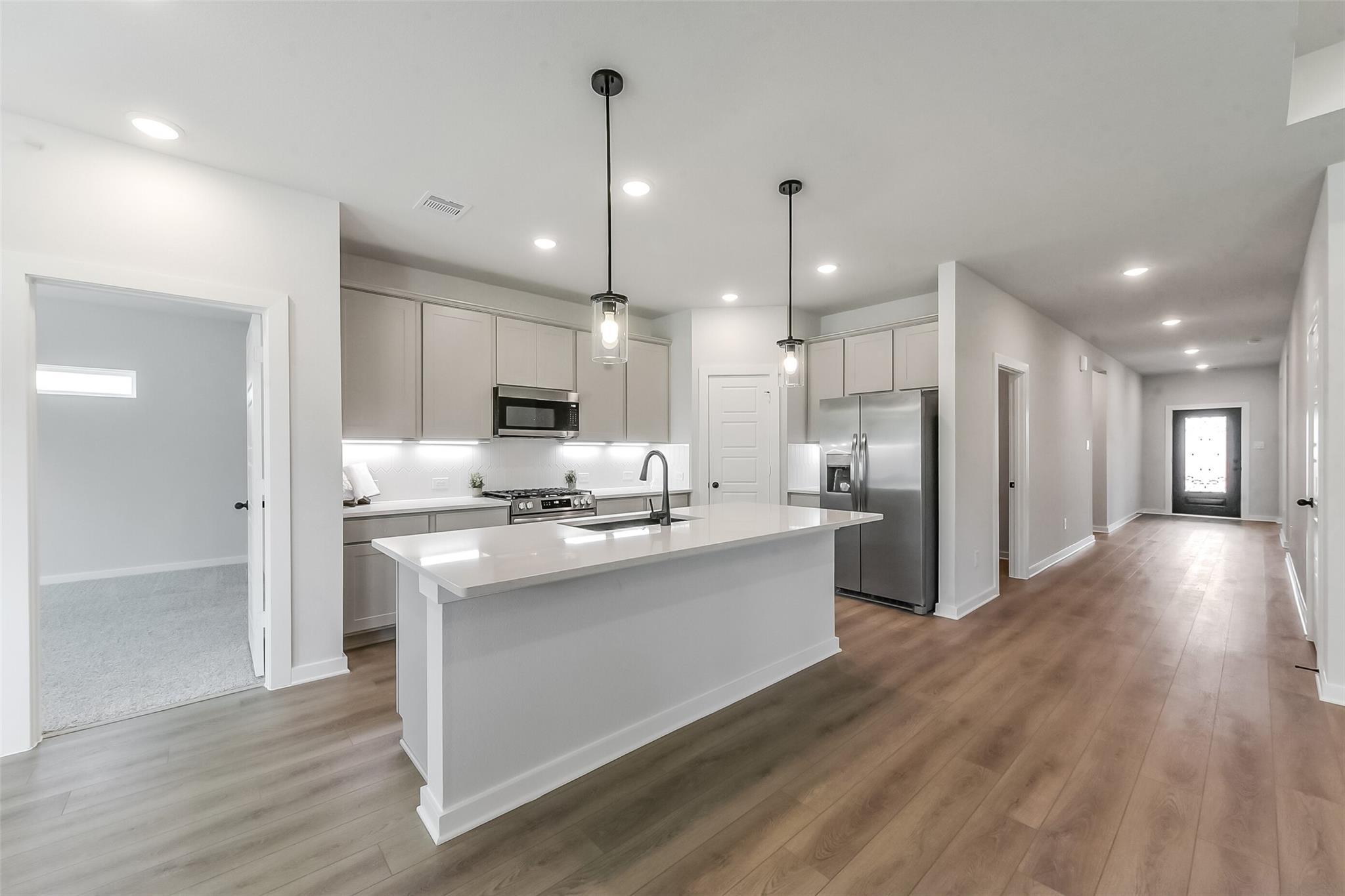 Modern white kitchen with quartz island, stainless appliances, pendant lights in The Everett C by Davidson Homes, Crosby TX