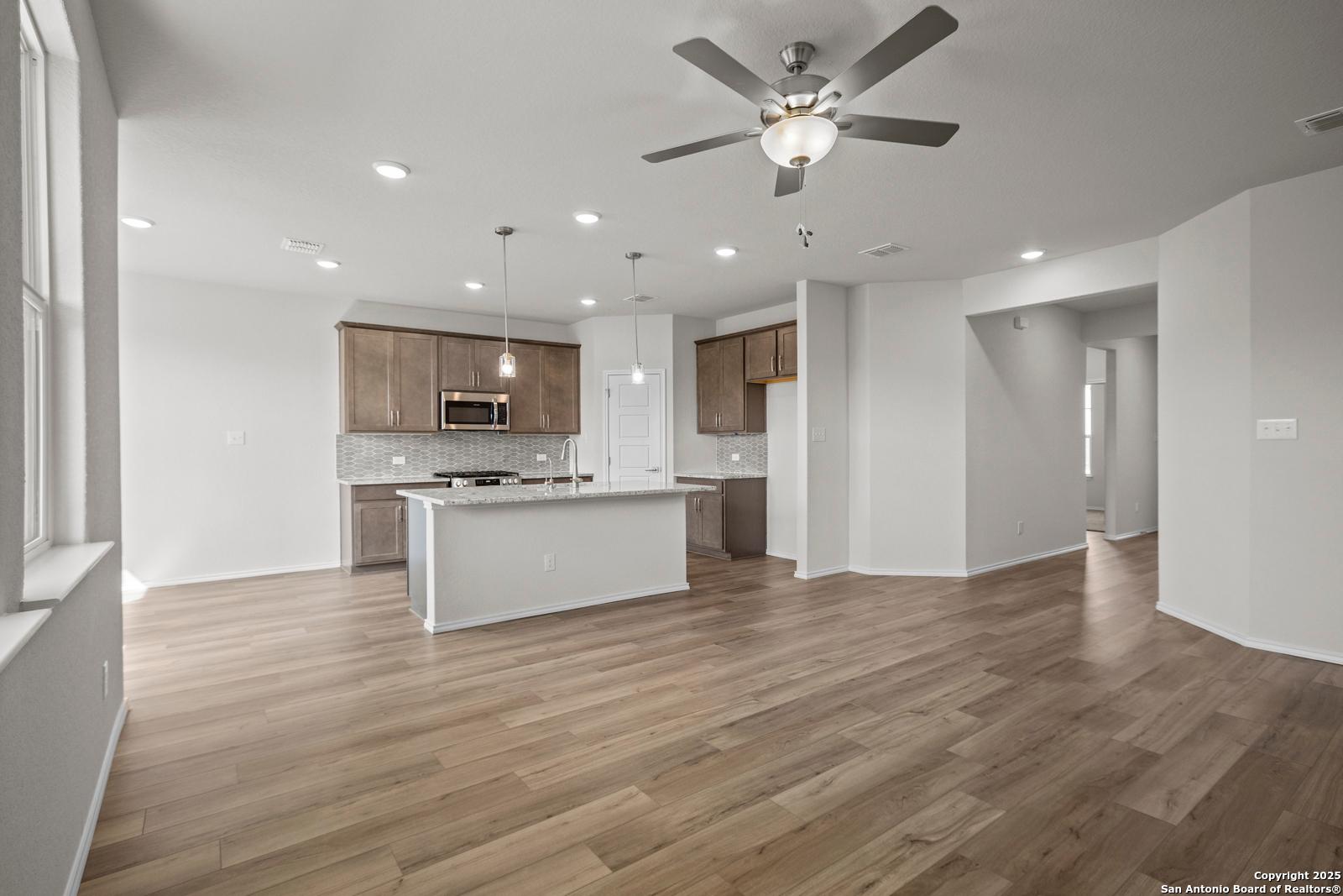 Open-concept kitchen with white island, wood cabinets, stainless appliances, and ceiling fans on hardwood floors in The Asheville J, San Antonio