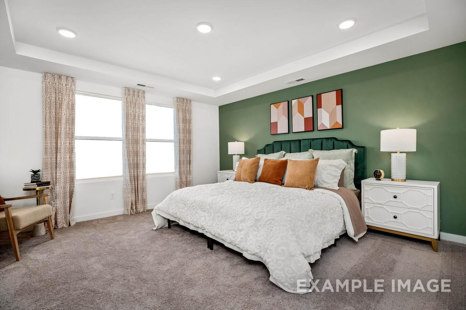 Spacious master bedroom in The Gordon C with king bed, green accent wall, abstract art, and large windows
