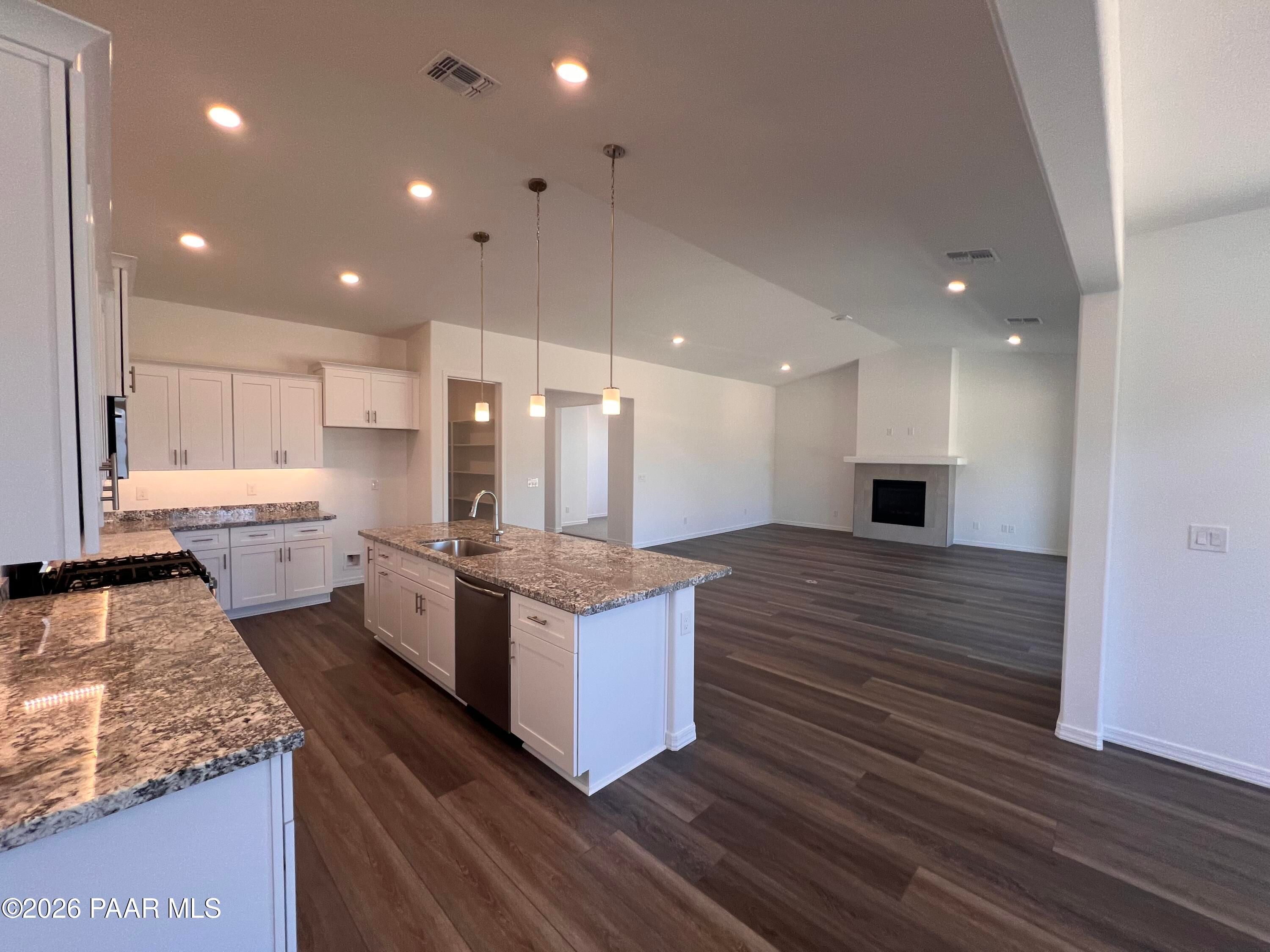 Modern open-concept kitchen with granite island, white cabinets, and stainless sink open to living room fireplace in Davidson Homes The Sunrise II A, Prescott AZ