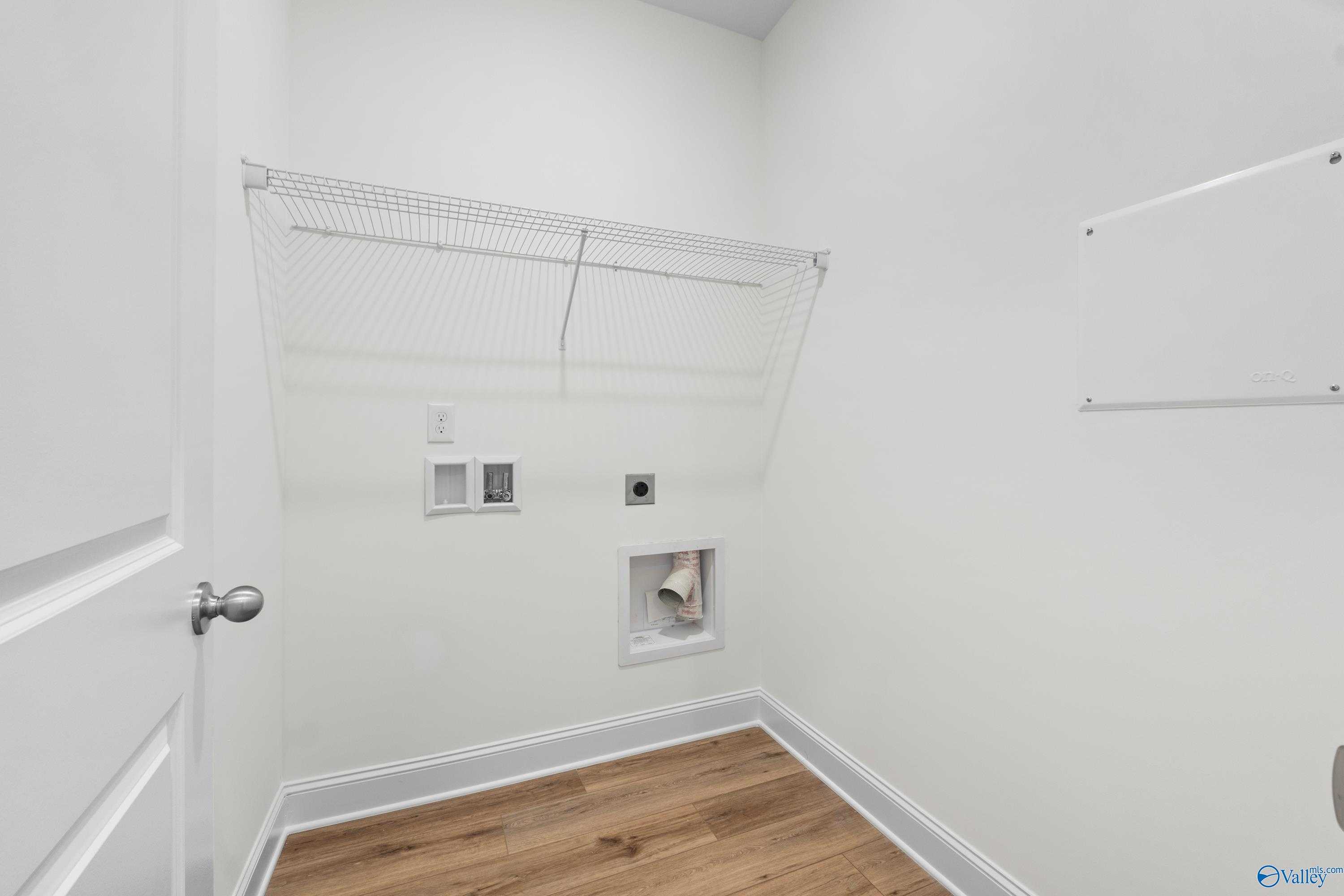 Bright white laundry room with wire shelving, washer-dryer hookups, hardwood floors in Davidson Homes The Asheville C, Athens, Alabama